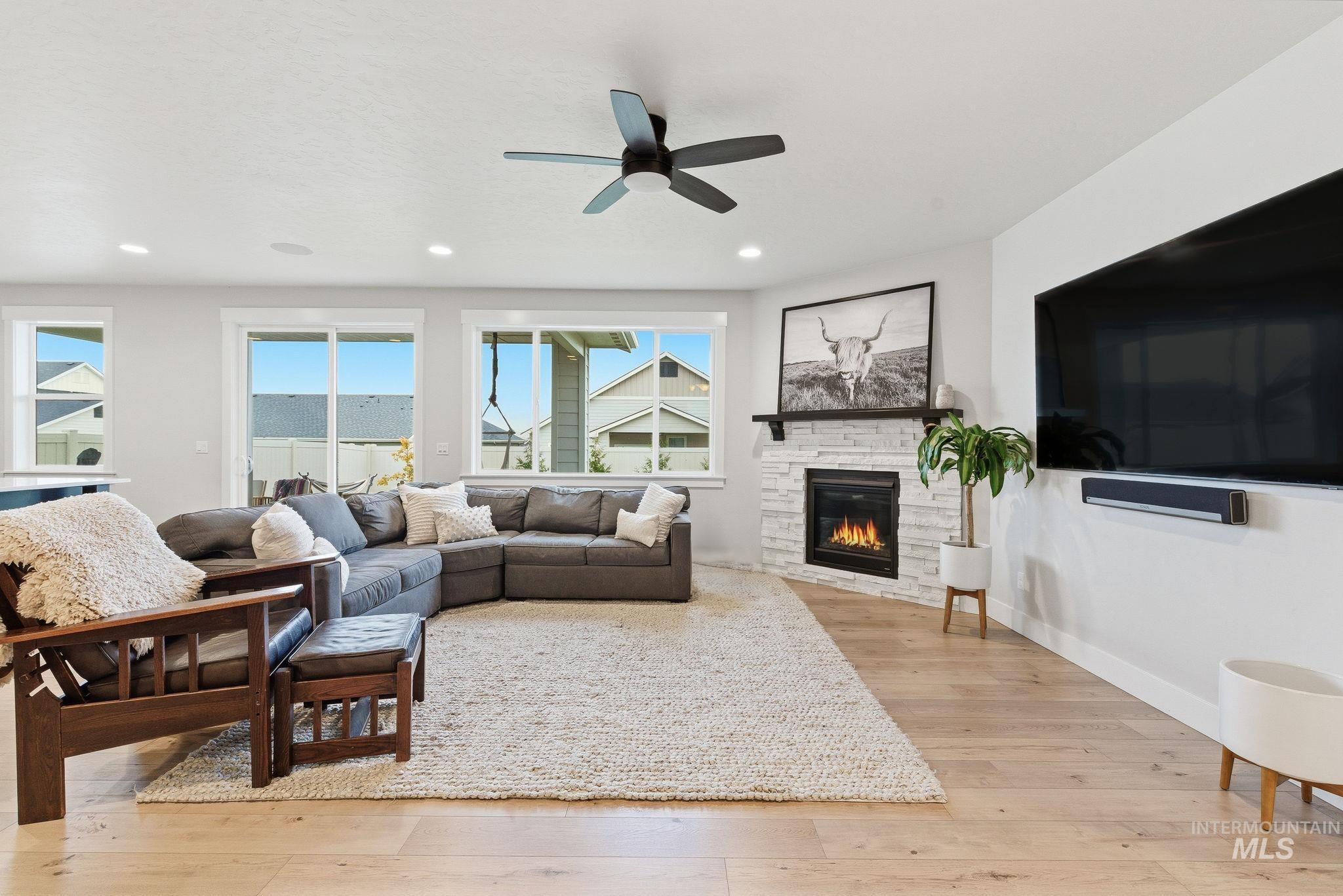 Living room featuring light wood finished floors, ceiling fan, a stone fireplace, and recessed lighting