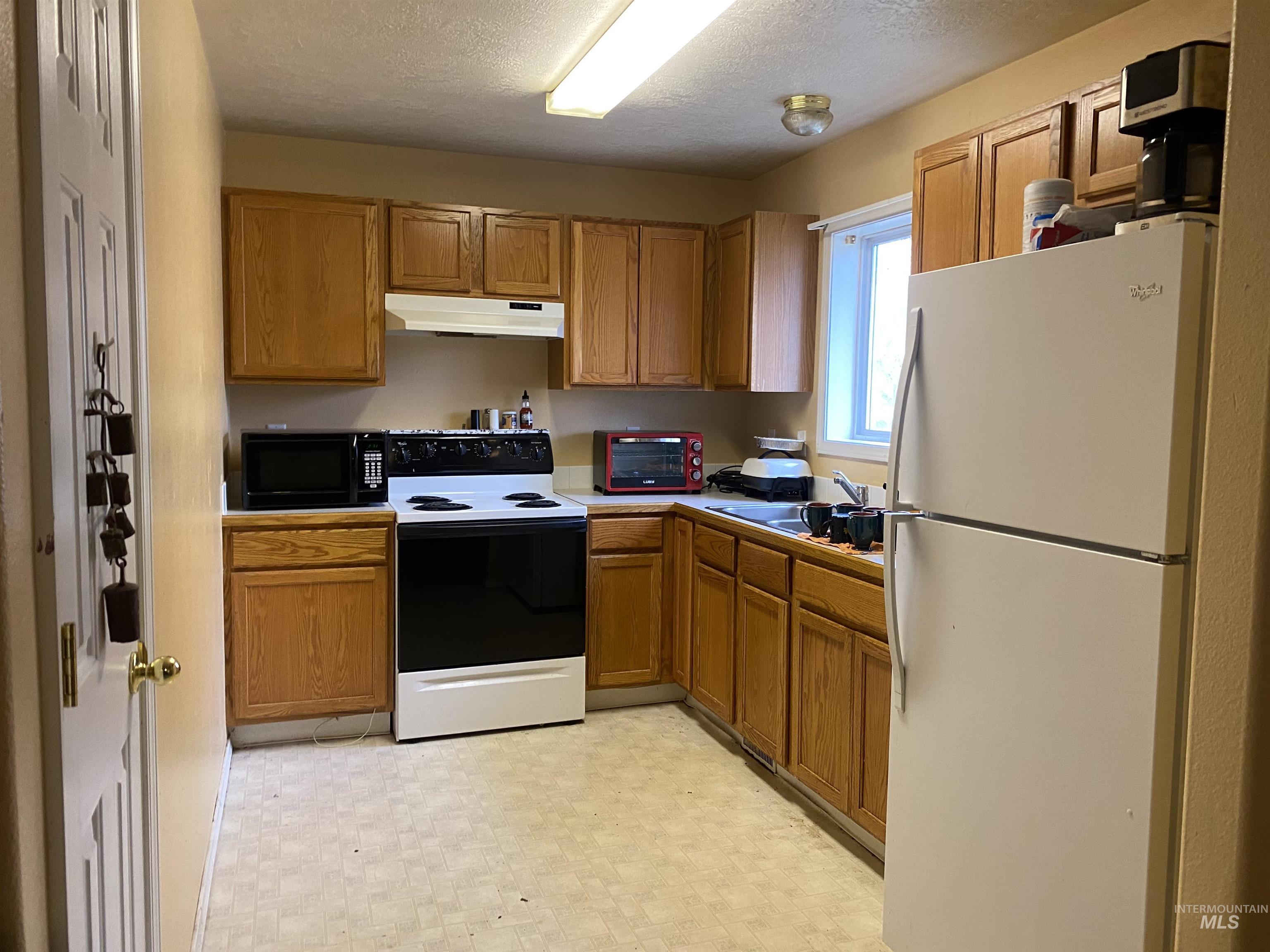 Kitchen with freestanding refrigerator, electric stove, brown cabinets, and a textured ceiling