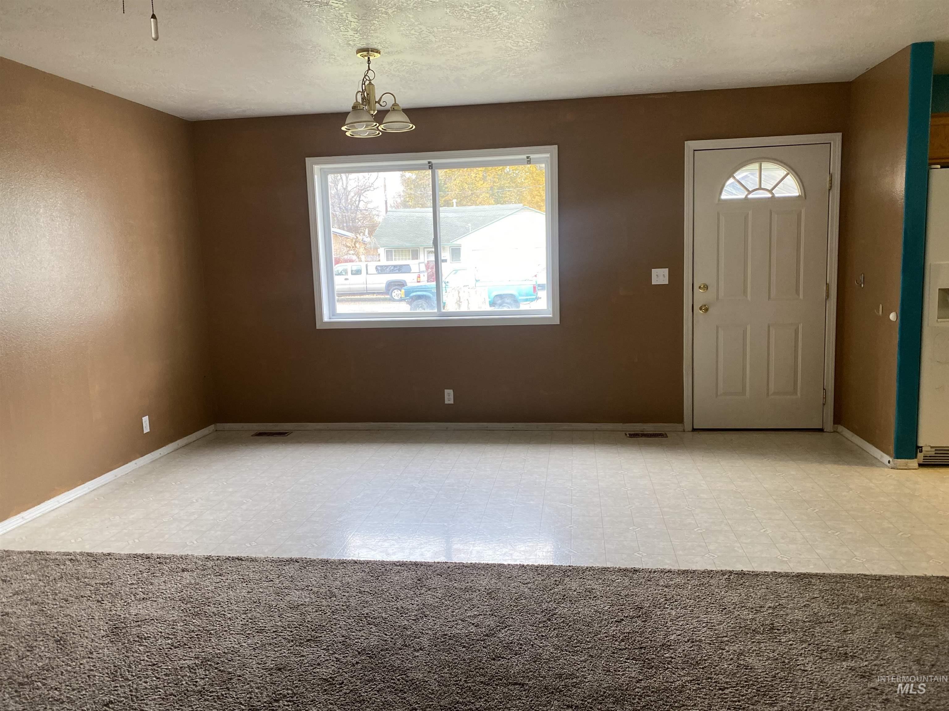 Entrance foyer featuring light flooring, a textured ceiling, light colored carpet, and a chandelier