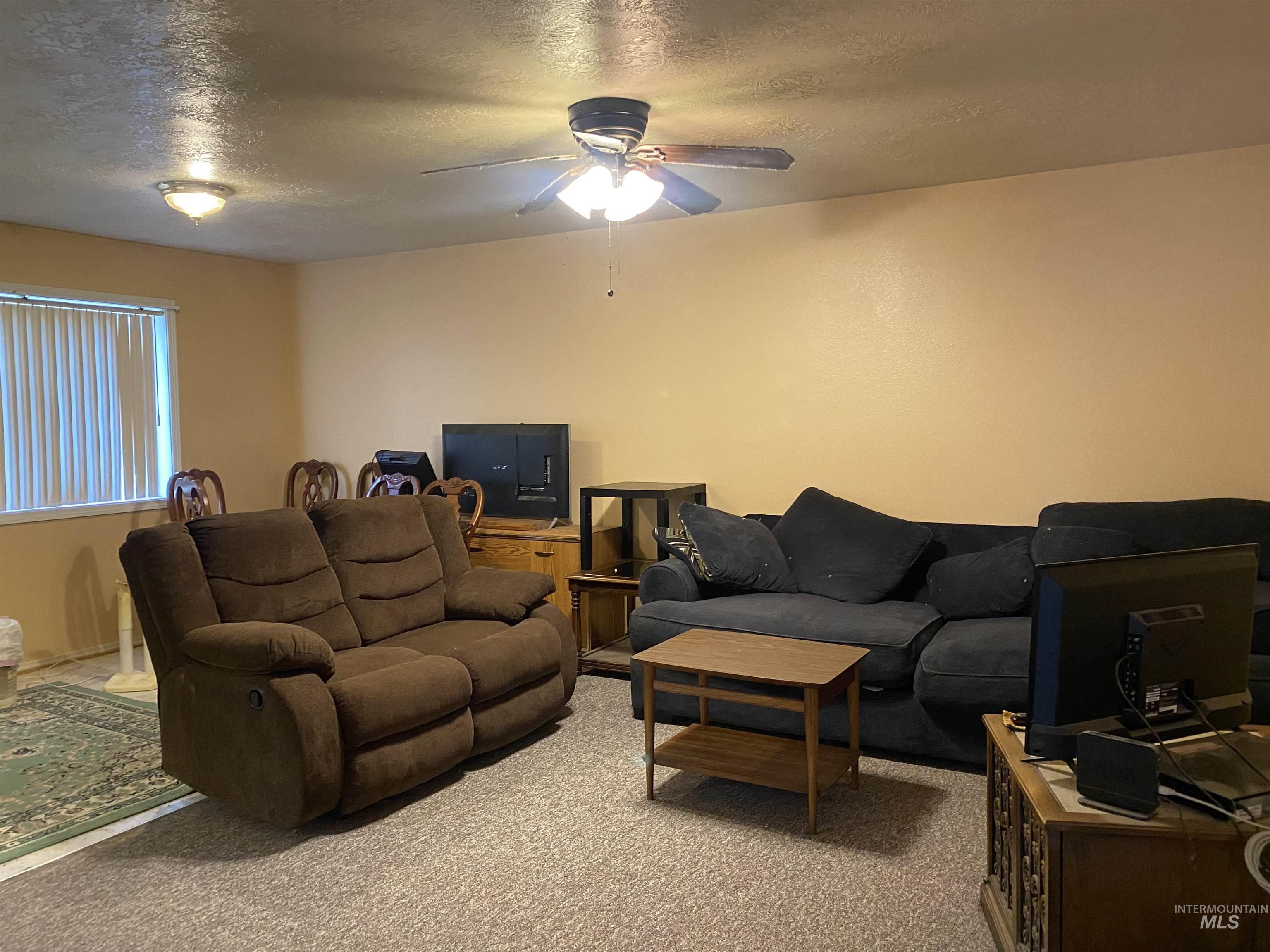 Carpeted living room with a textured ceiling and ceiling fan
