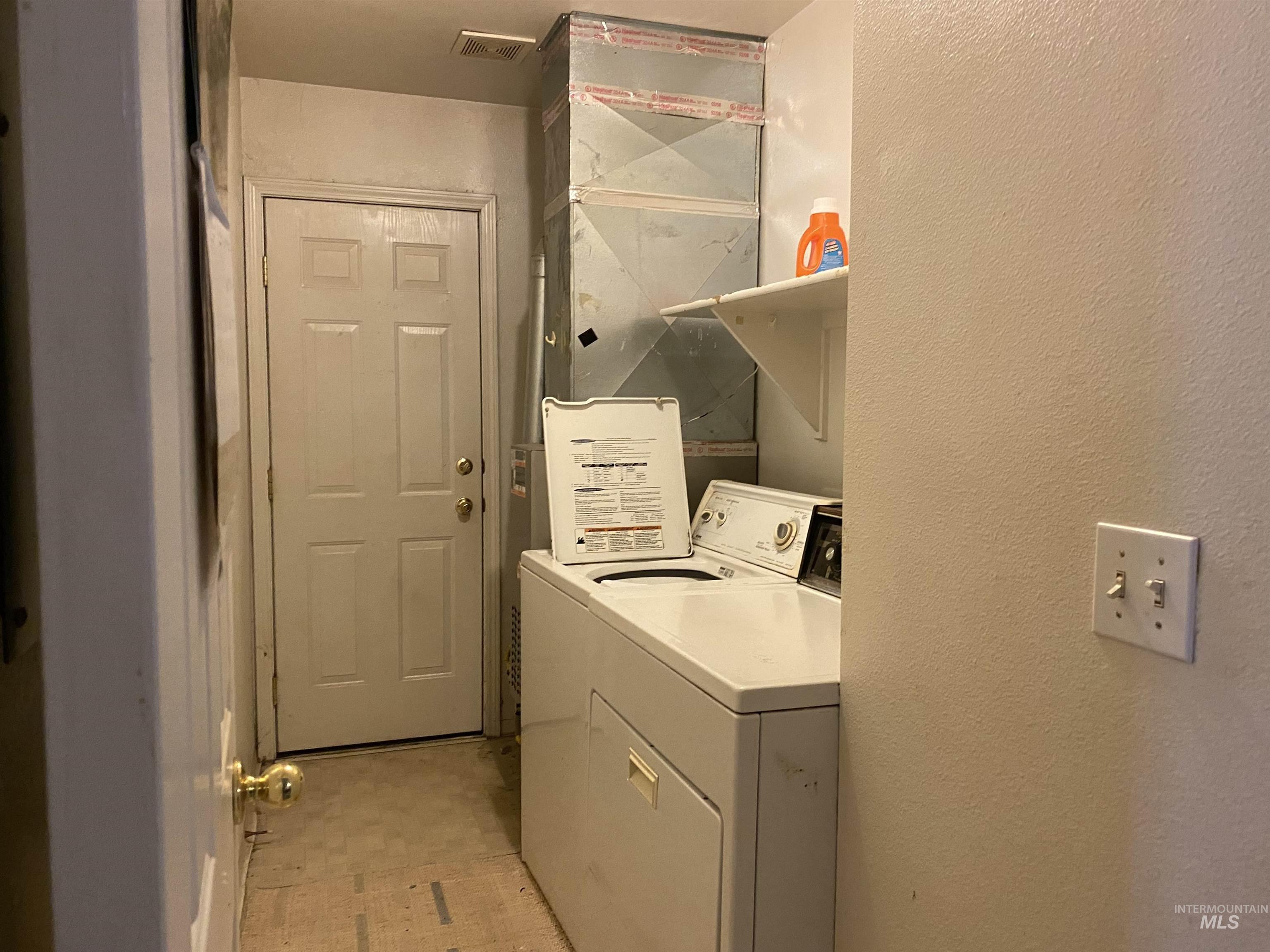 Laundry room with washing machine and dryer, a textured wall, heating unit, and light flooring