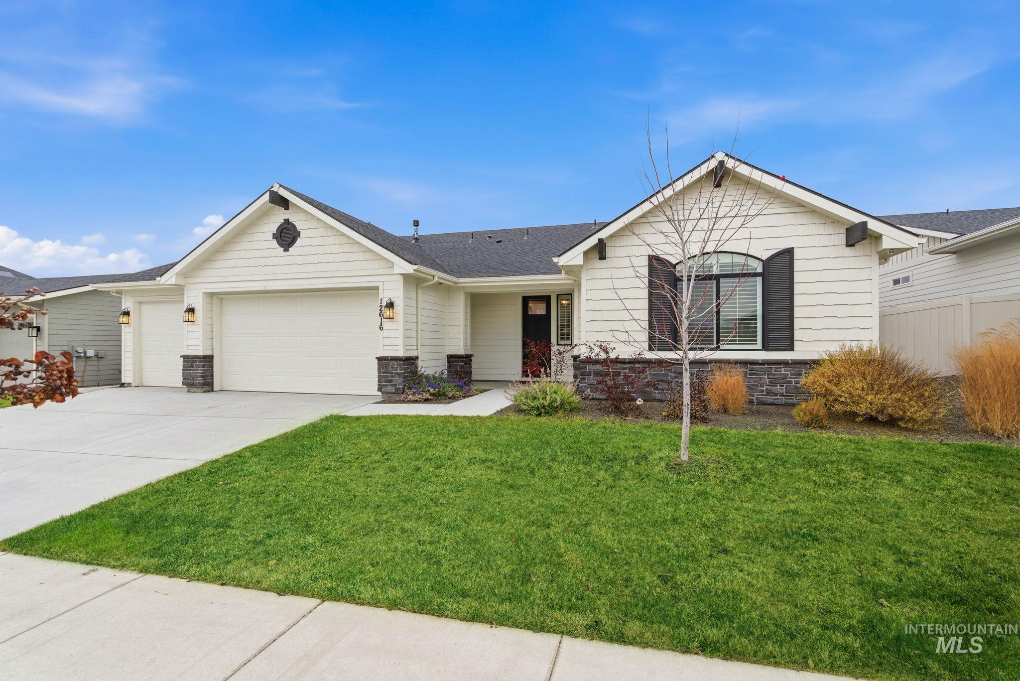 Ranch-style home featuring stone siding, driveway, an attached garage, and roof with shingles