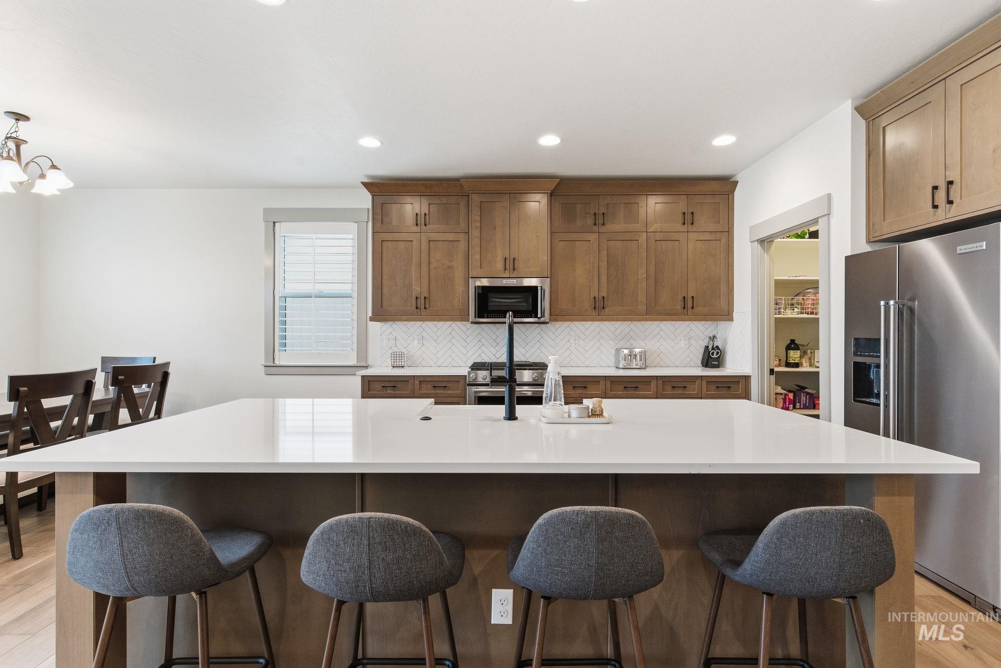 Kitchen featuring light wood-type flooring, appliances with stainless steel finishes, backsplash, recessed lighting, and a kitchen island with sink