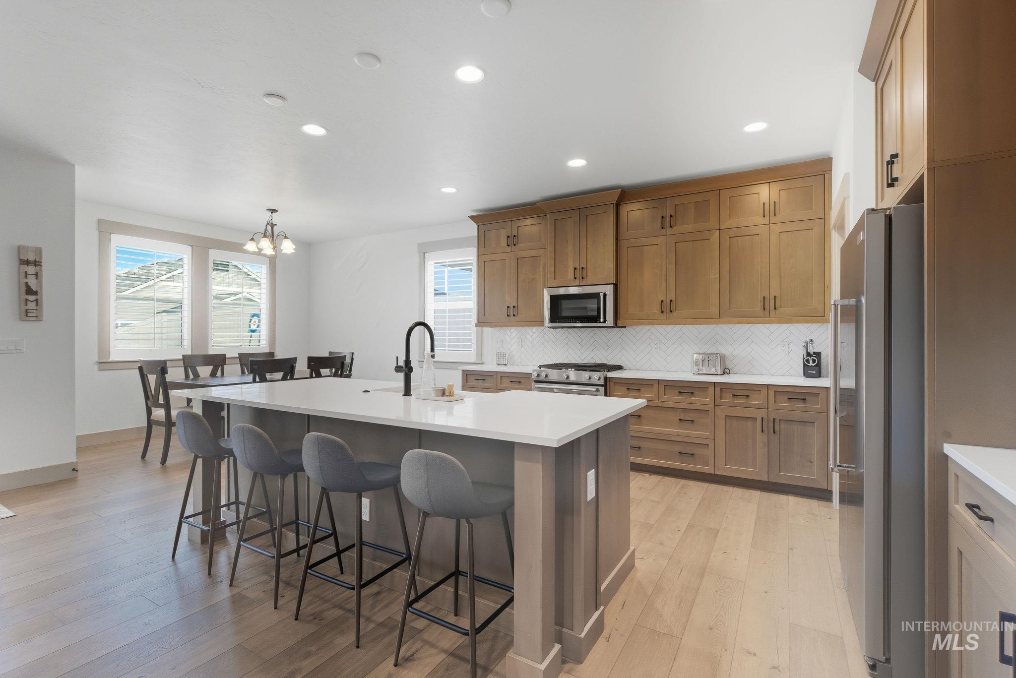 Kitchen featuring brown cabinetry, backsplash, a center island with sink, stainless steel appliances, and recessed lighting