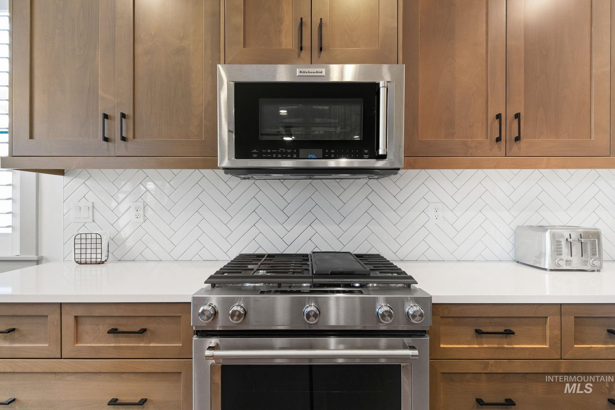 Kitchen featuring appliances with stainless steel finishes, decorative backsplash, brown cabinetry, and light stone countertops