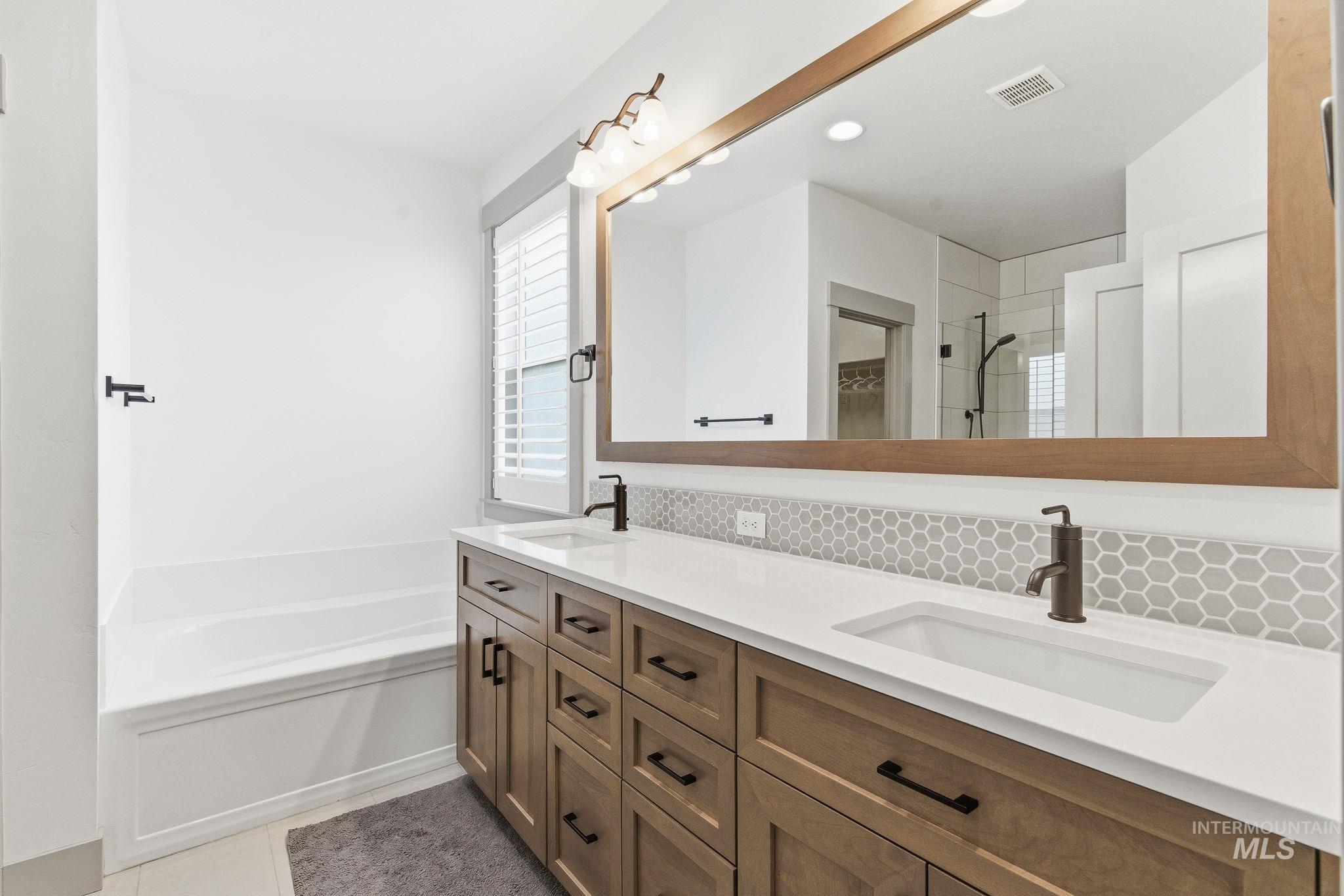 Bathroom with double vanity, decorative backsplash, light tile patterned floors, a bath, and a tile shower