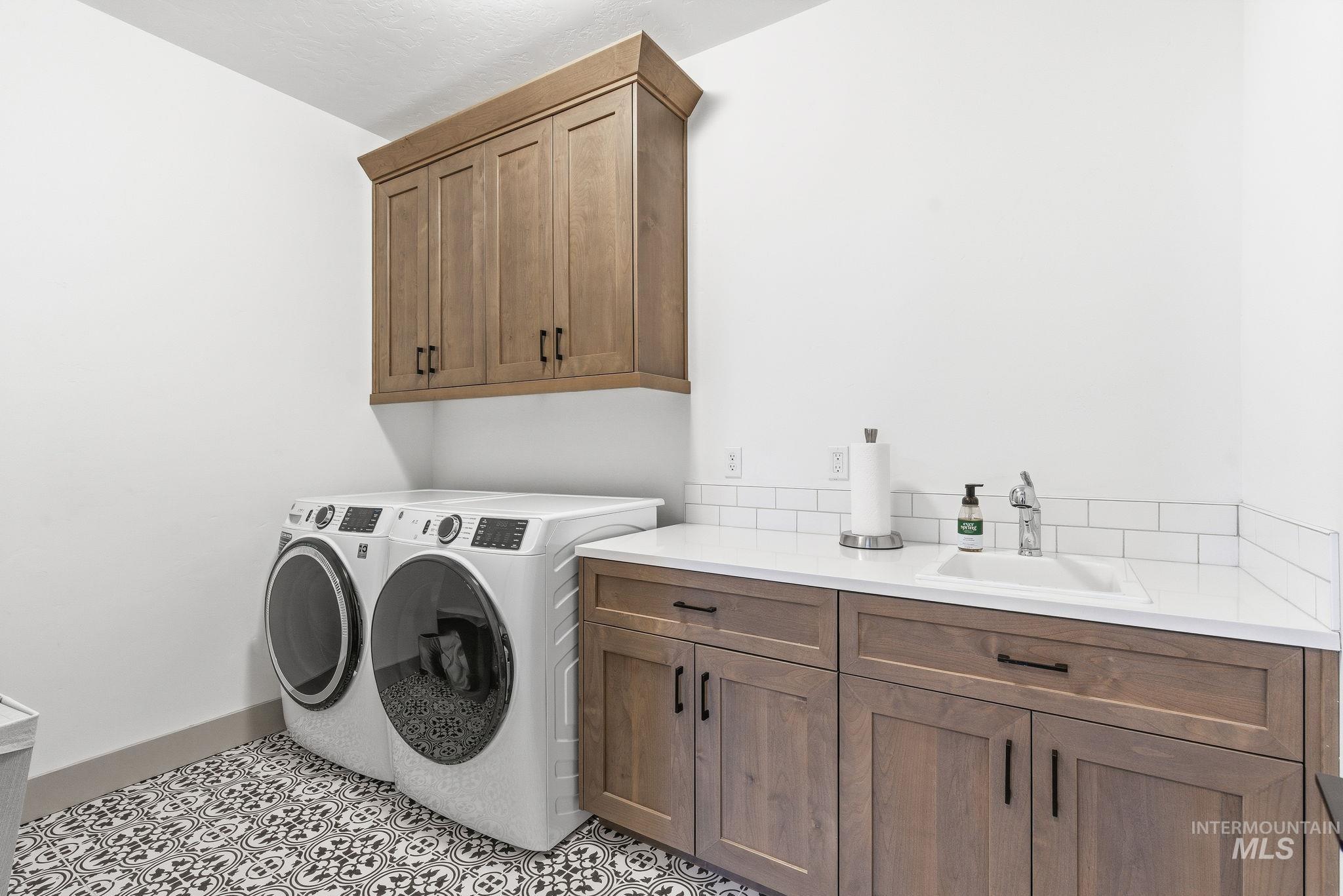 Laundry area featuring separate washer and dryer, light tile patterned floors, and cabinet space