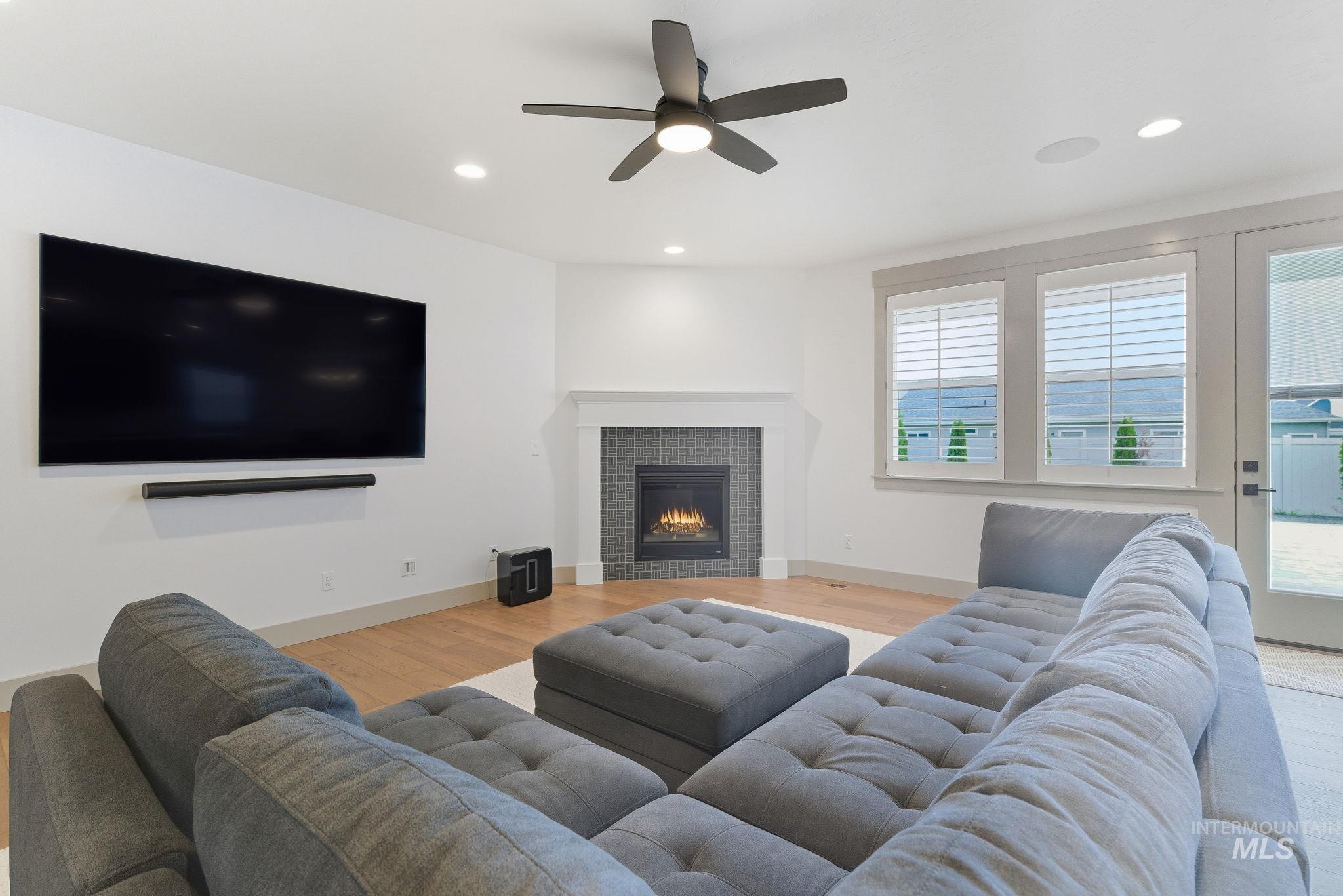 Living room featuring recessed lighting, light wood-type flooring, a tiled fireplace, and a ceiling fan