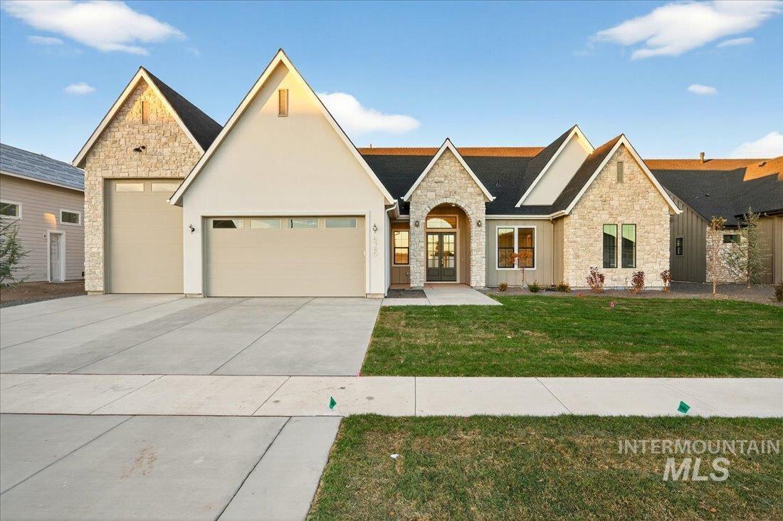 View of front of property featuring stone siding, a front lawn, an attached garage, concrete driveway, and stucco siding
