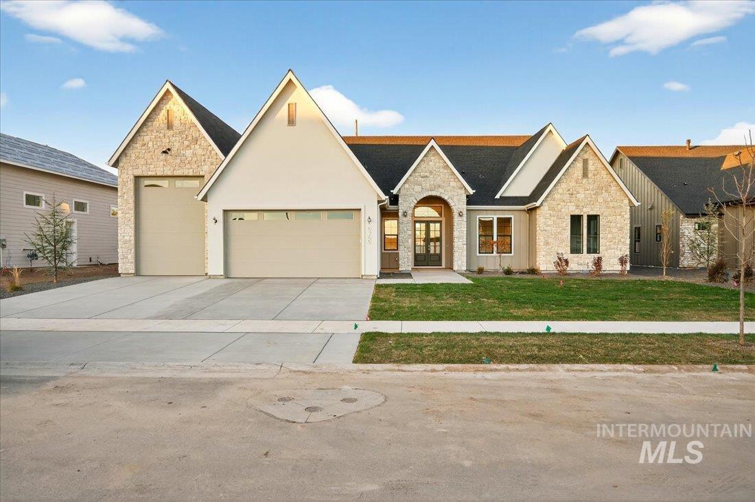 View of front of home featuring stone siding, a front yard, driveway, a garage, and stucco siding