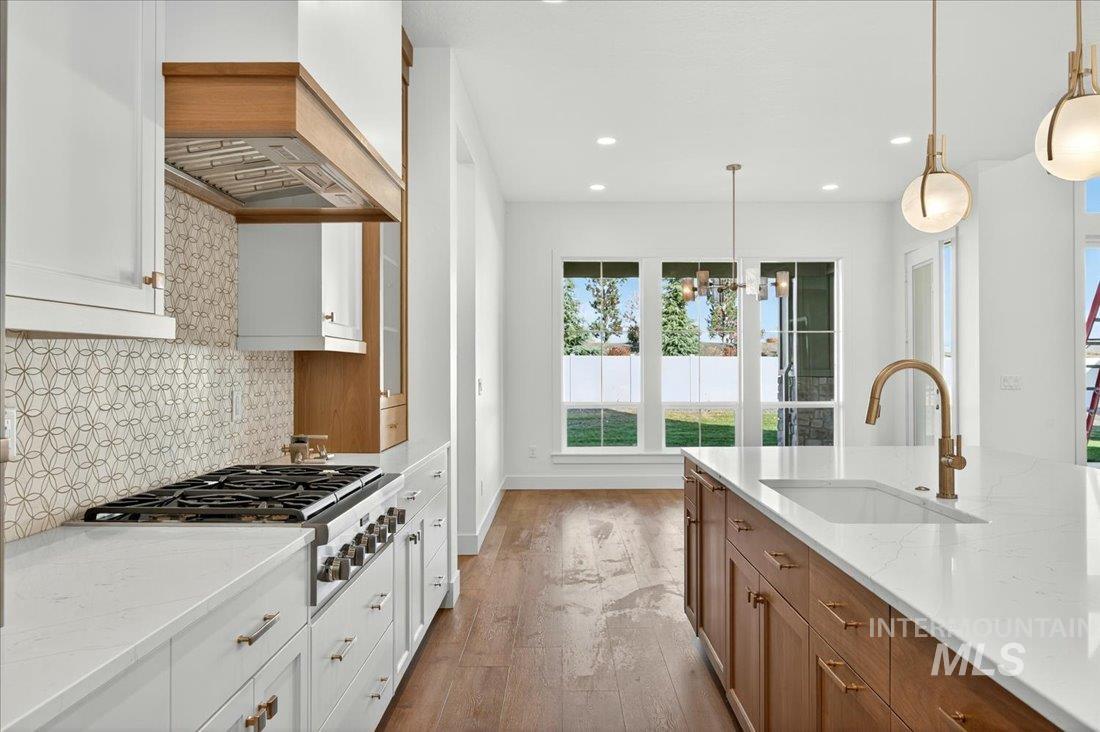 Kitchen featuring hanging light fixtures, brown cabinetry, light stone counters, tasteful backsplash, and stainless steel gas cooktop
