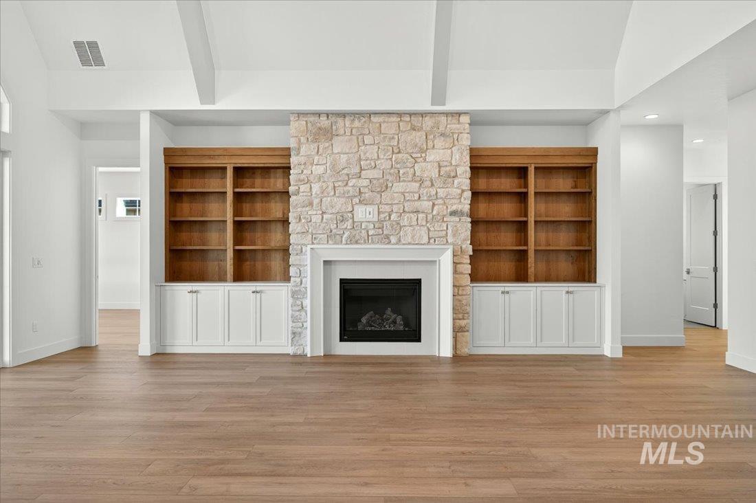 Unfurnished living room featuring beam ceiling, light wood-style flooring, a stone fireplace, recessed lighting, and high vaulted ceiling