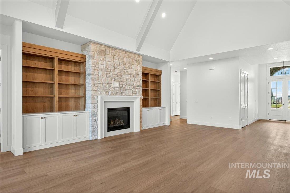 Unfurnished living room featuring high vaulted ceiling, light wood finished floors, a stone fireplace, recessed lighting, and french doors