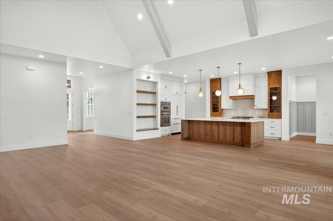 Kitchen featuring brown cabinets, beam ceiling, open floor plan, light countertops, and a spacious island