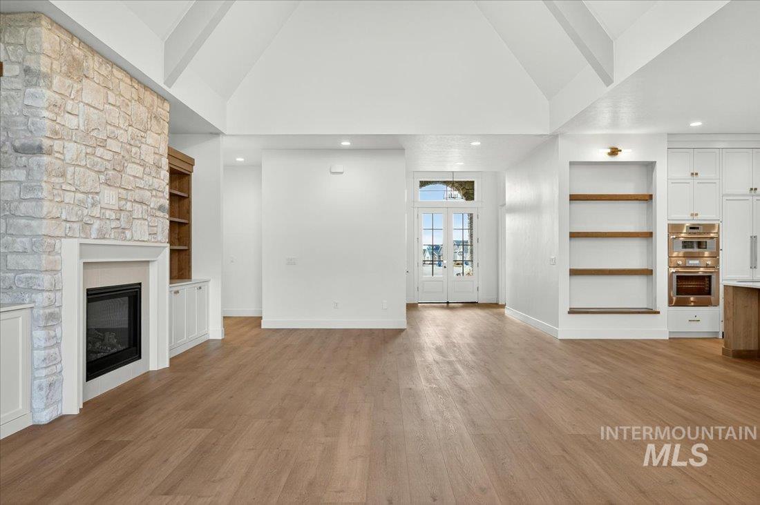 Unfurnished living room featuring built in shelves, high vaulted ceiling, light wood-style flooring, a large fireplace, and recessed lighting