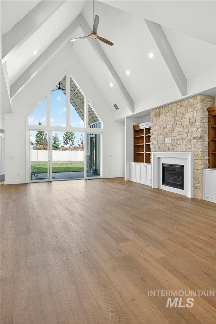 Unfurnished living room with high vaulted ceiling, beam ceiling, light wood-style floors, a glass covered fireplace, and built in shelves