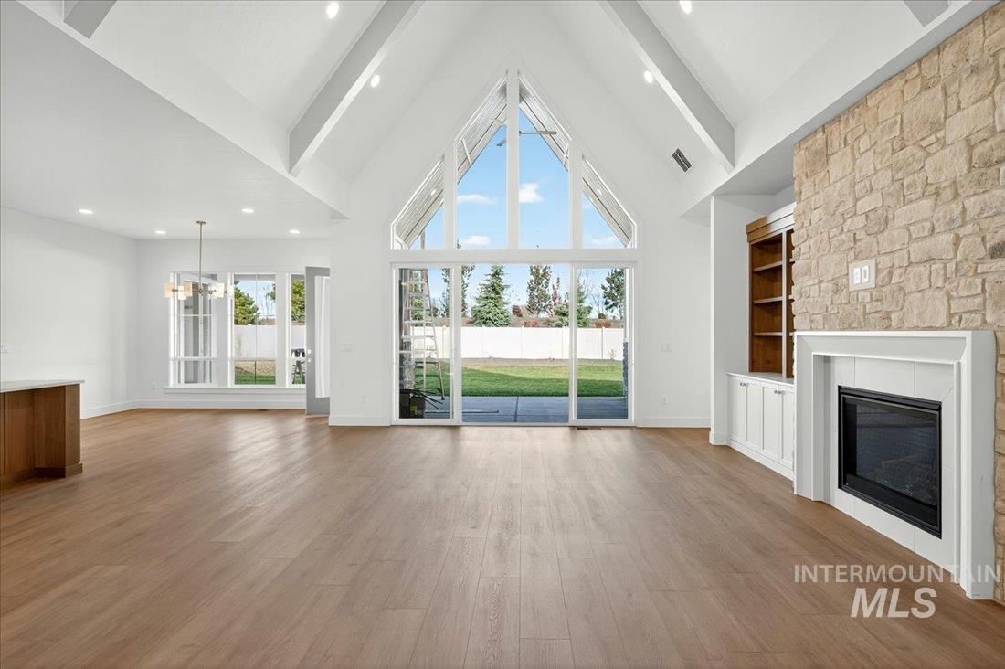 Unfurnished living room with high vaulted ceiling, a glass covered fireplace, light wood finished floors, built in shelves, and beam ceiling