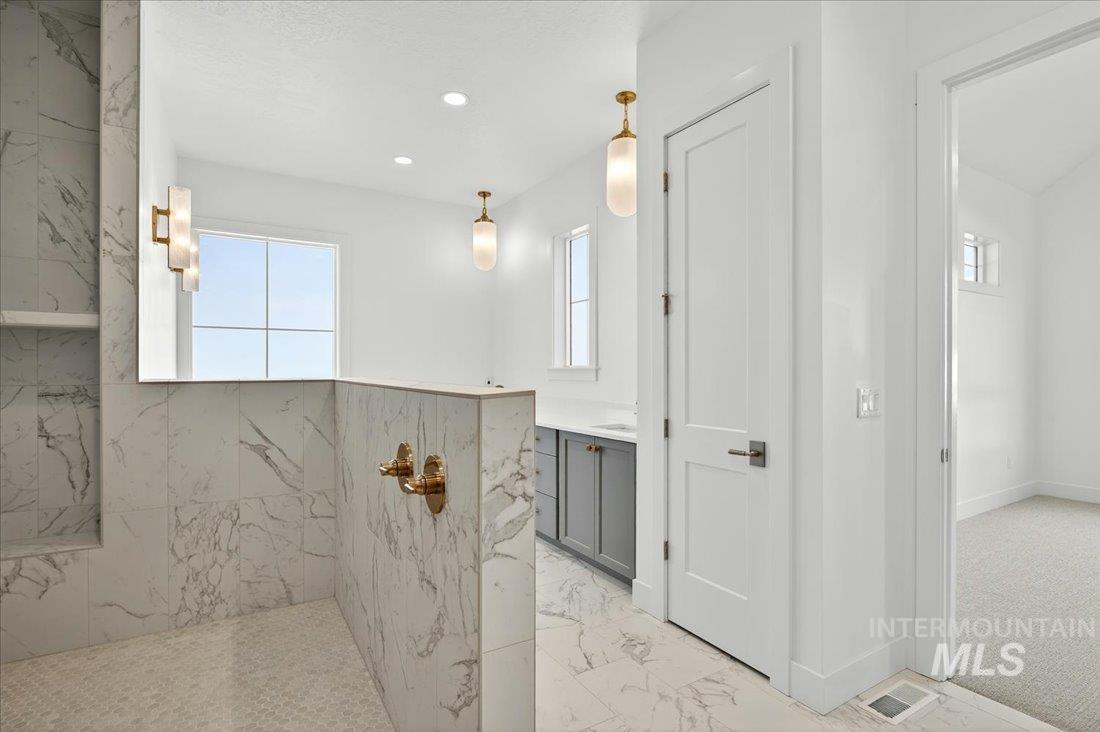 Bathroom featuring vanity, plenty of natural light, light marble finish flooring, recessed lighting, and a marble finish shower
