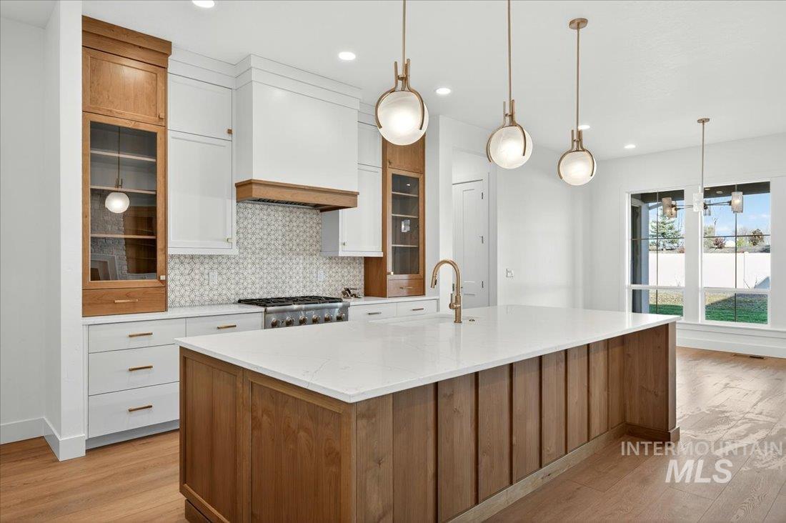 Kitchen with brown cabinetry, glass insert cabinets, tasteful backsplash, white cabinetry, and recessed lighting