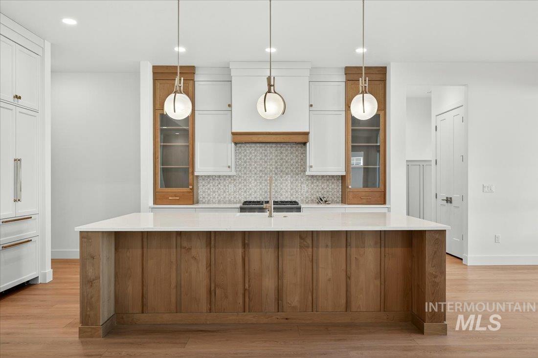 Kitchen featuring white cabinetry, a large island, brown cabinetry, hanging light fixtures, and glass insert cabinets
