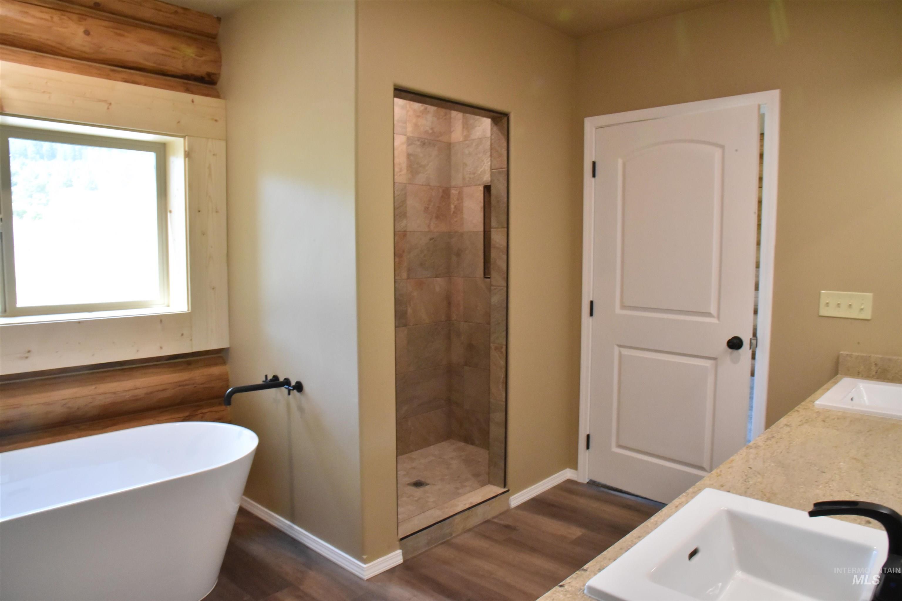 Full bath with dark wood-style flooring, a soaking tub, double vanity, and a shower stall