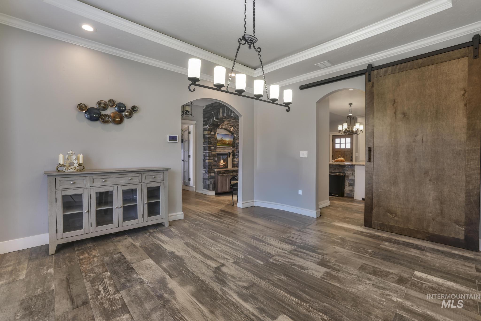Dining area with arched walkways, dark wood-style flooring, a chandelier, ornamental molding, and a barn door