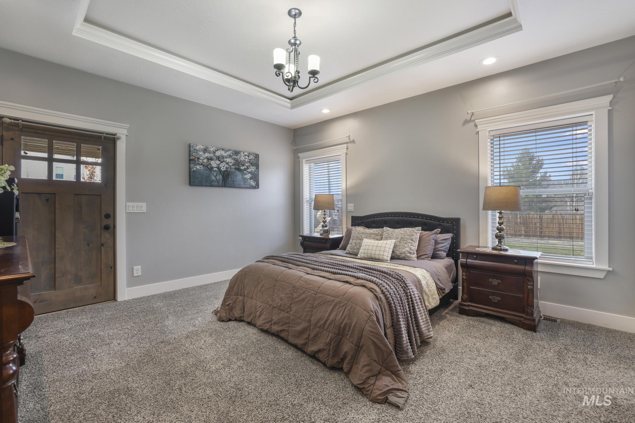 Carpeted bedroom with multiple windows, a raised ceiling, a chandelier, and recessed lighting