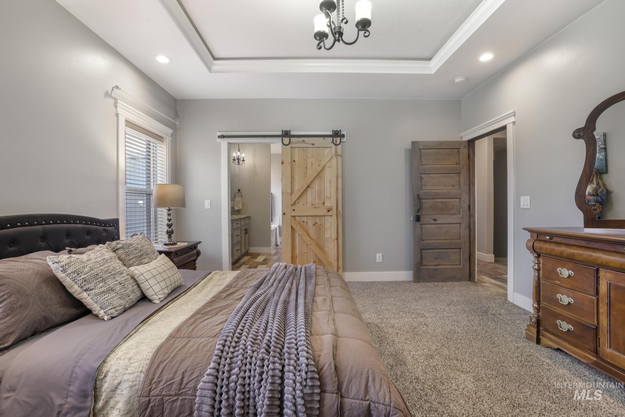 Carpeted bedroom featuring a barn door, a tray ceiling, recessed lighting, connected bathroom, and a chandelier
