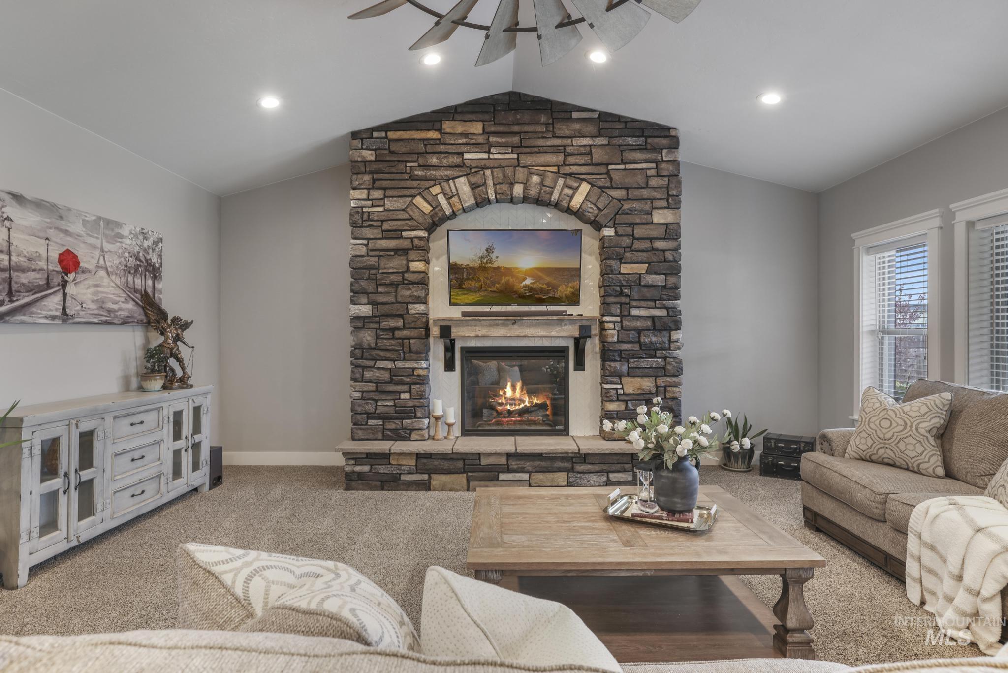 Carpeted living area featuring a ceiling fan, lofted ceiling, a fireplace, and recessed lighting