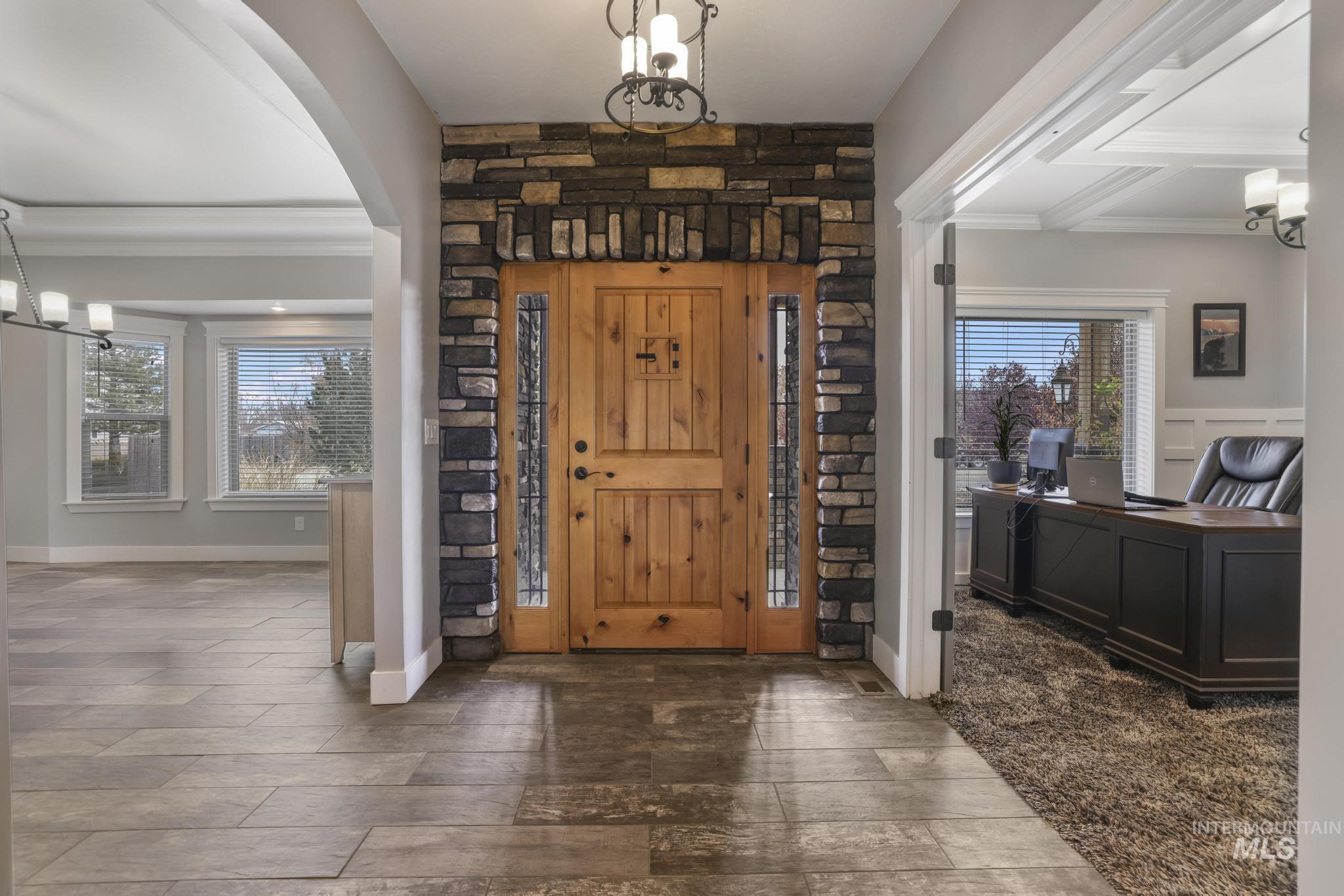 Foyer entrance with a chandelier, ornamental molding, wood finished floors, and arched walkways
