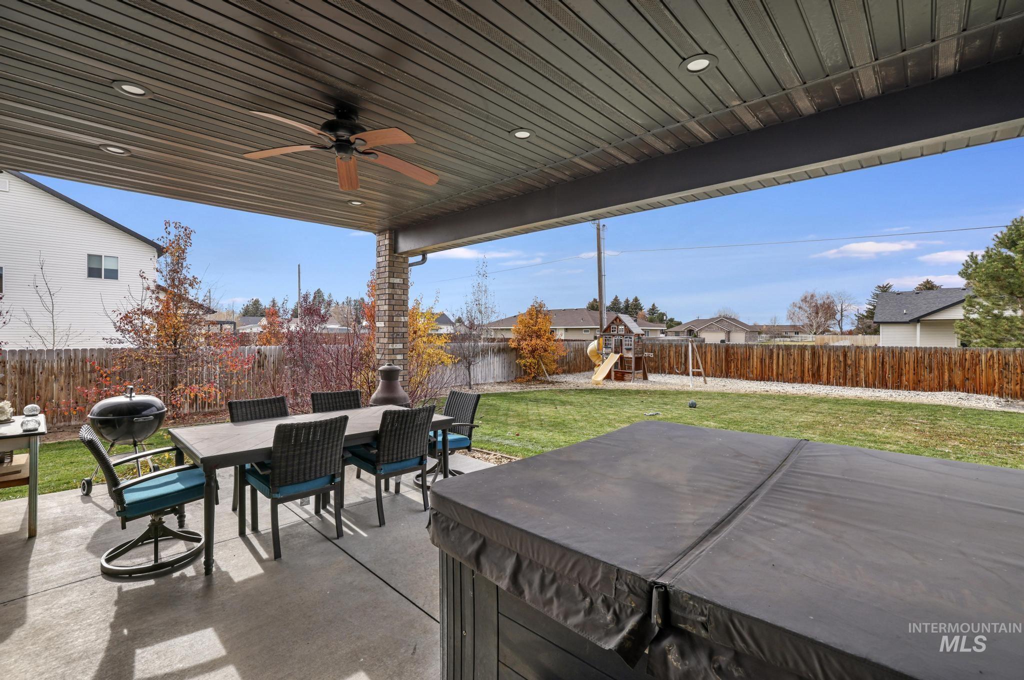 Fenced backyard featuring outdoor dining space, a playground, a patio area, a hot tub, and a ceiling fan