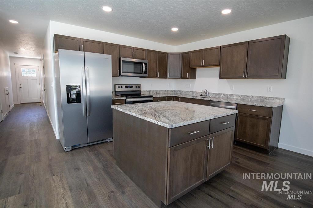 Kitchen featuring dark brown cabinets, stainless steel appliances, recessed lighting, dark wood-style floors, and light stone countertops