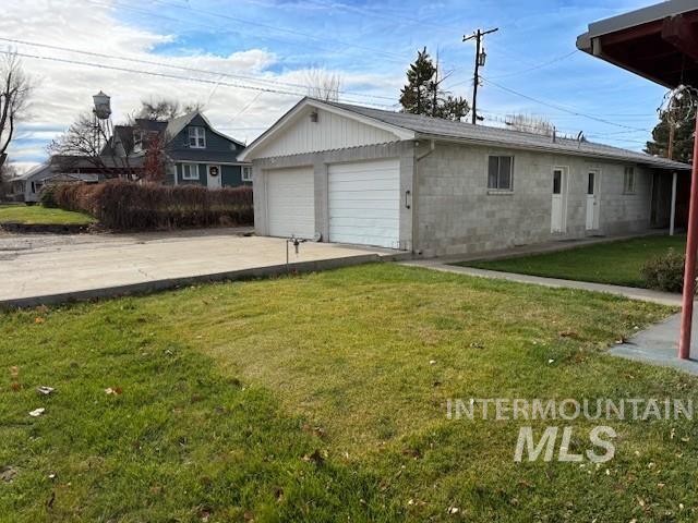 View of side of property with concrete block siding, a lawn, a garage, and an outbuilding
