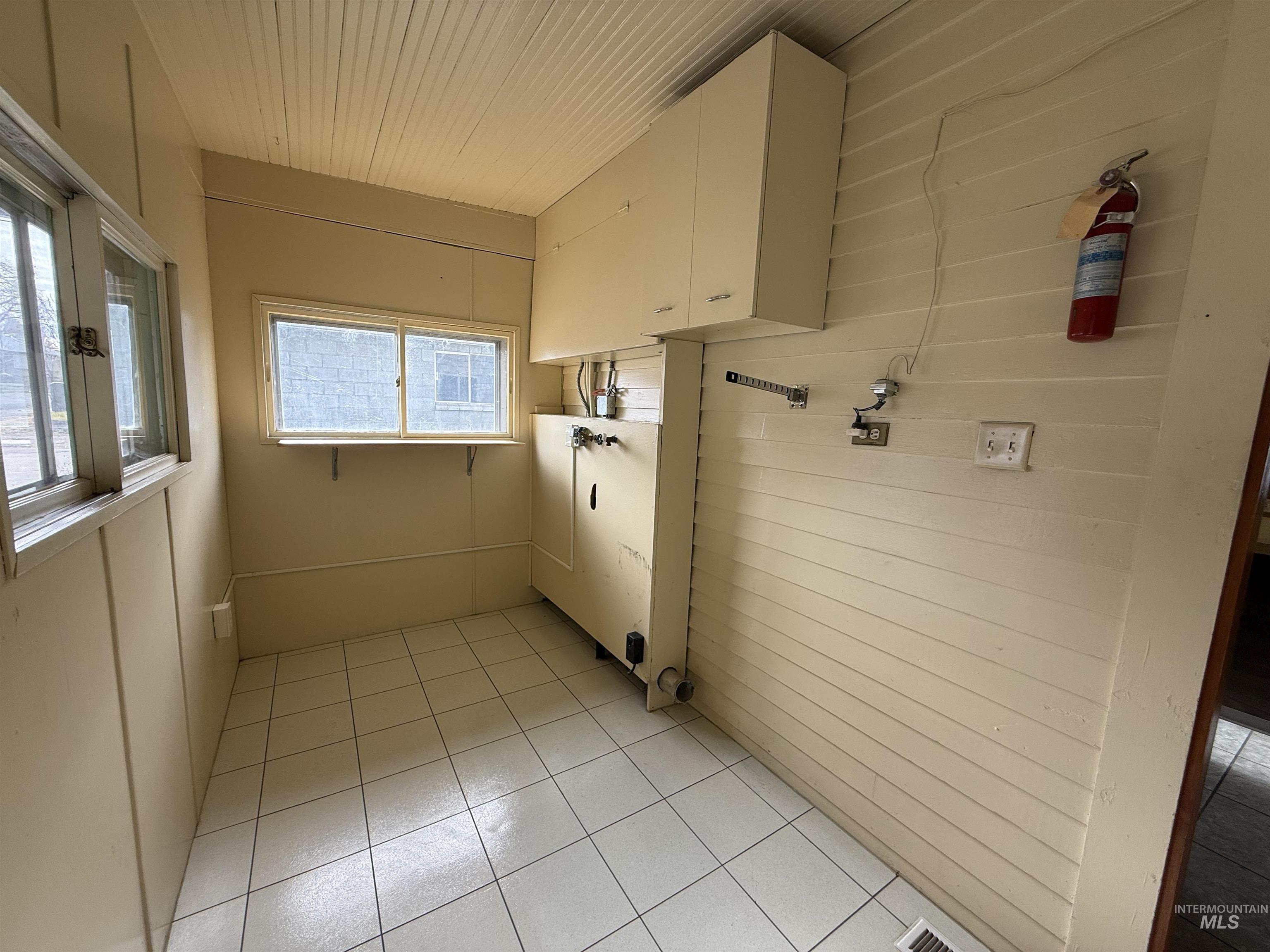 Laundry room with light tile patterned flooring, wood walls, and cabinet space