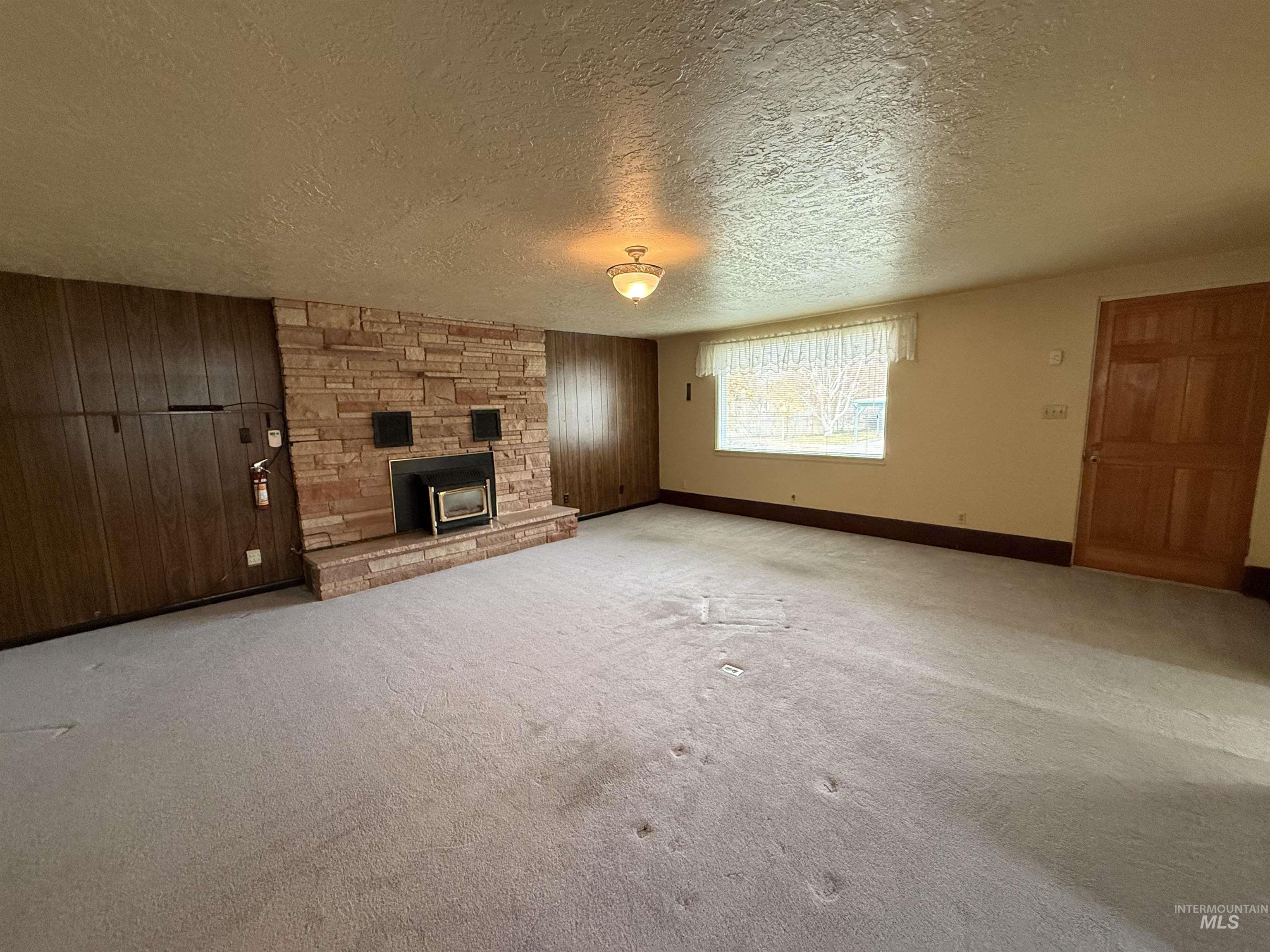 Unfurnished living room featuring wood walls, carpet, a textured ceiling, and a stone fireplace