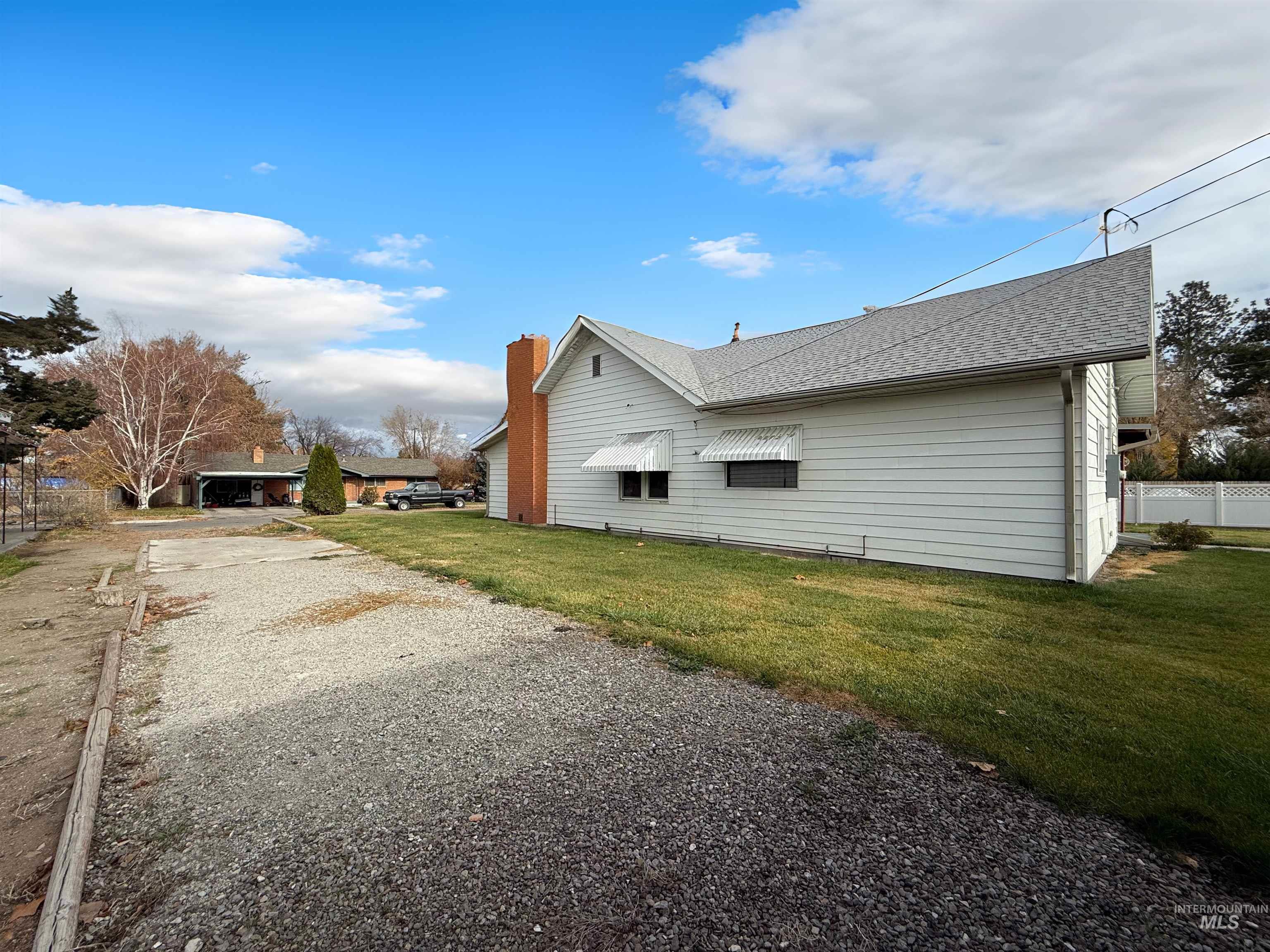 View of side of property with roof with shingles, gravel driveway, and a chimney
