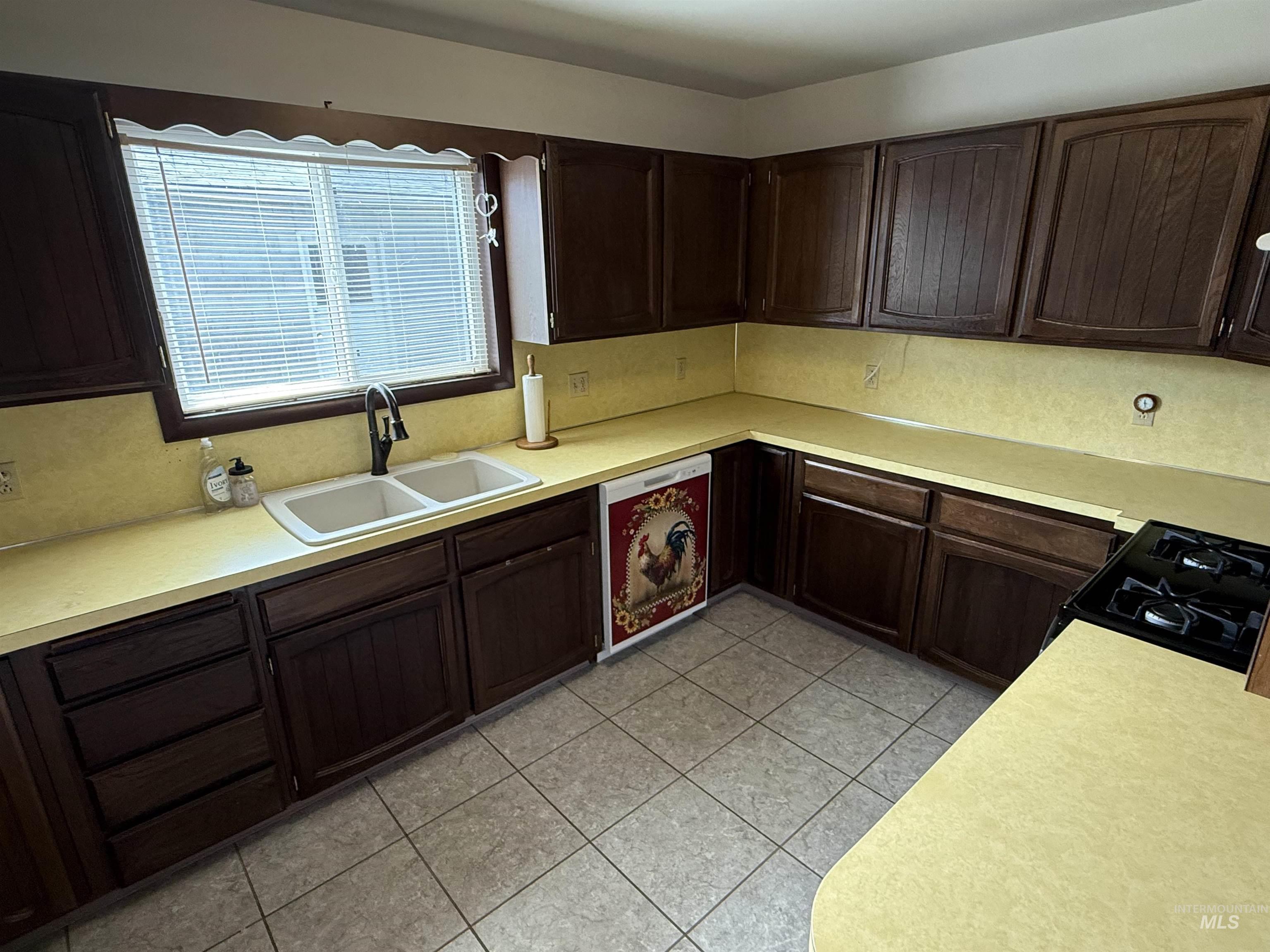 Kitchen with dark brown cabinetry, light countertops, dishwashing machine, and light tile patterned floors