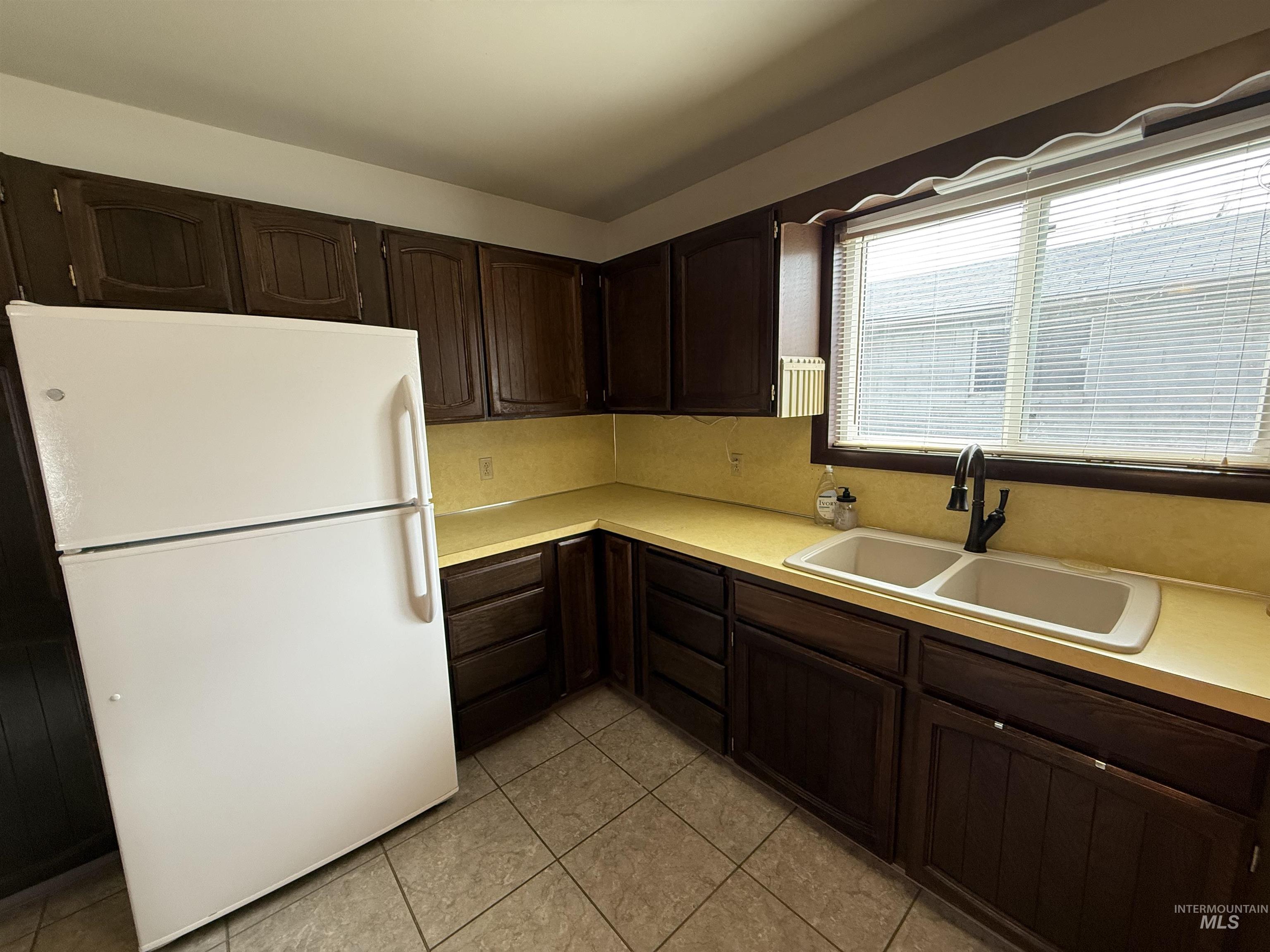 Kitchen with freestanding refrigerator, light countertops, dark brown cabinetry, and light tile patterned flooring