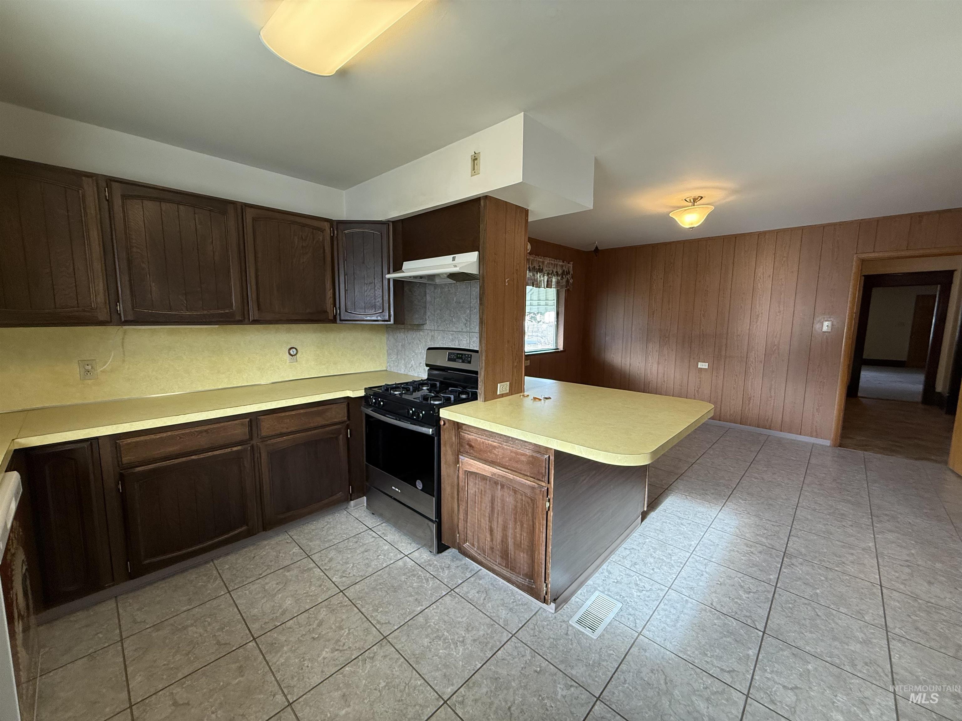 Kitchen featuring dark brown cabinetry, stainless steel gas range oven, light countertops, under cabinet range hood, and dishwashing machine