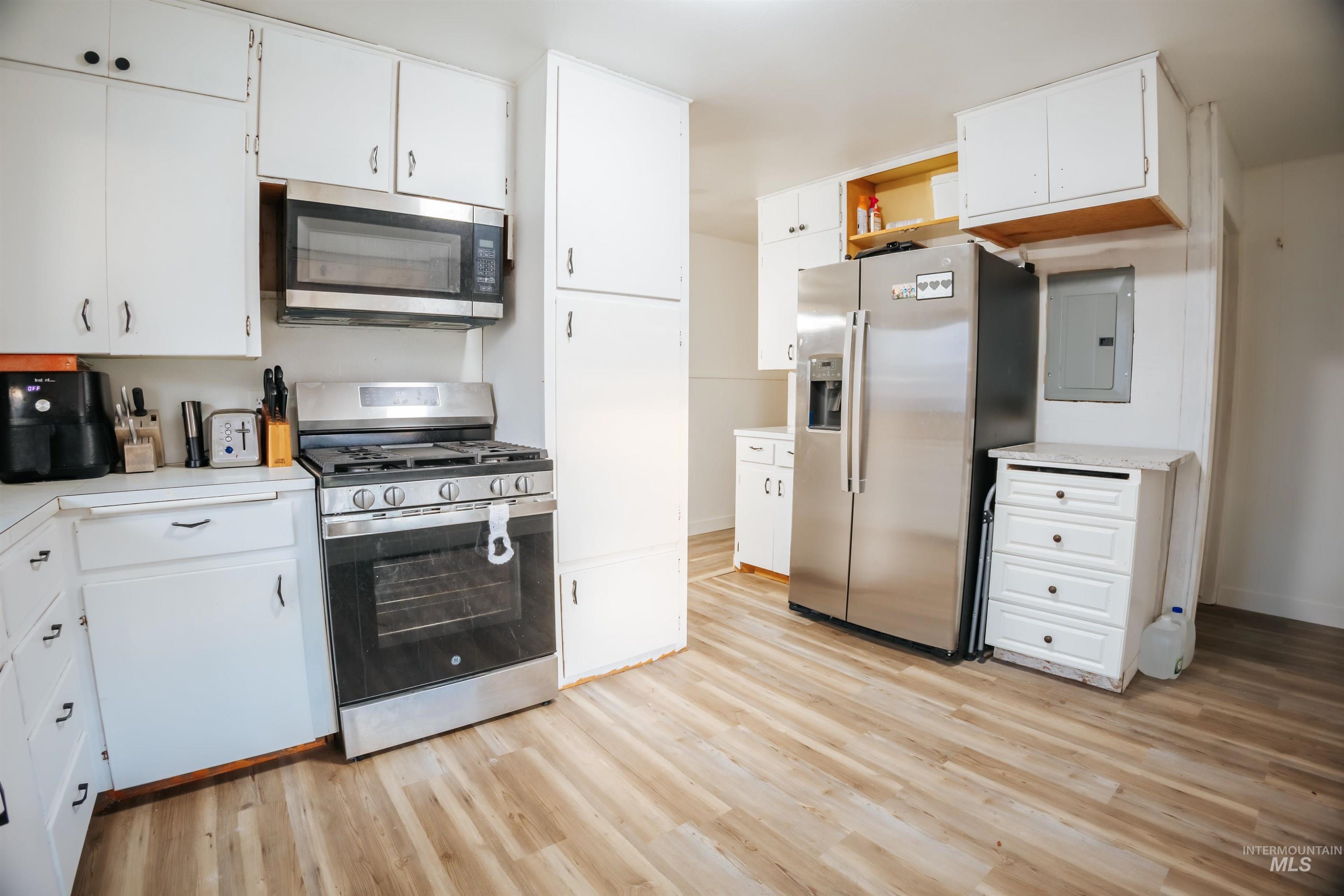 Kitchen with stainless steel appliances, light countertops, white cabinetry, light wood finished floors, and electric panel