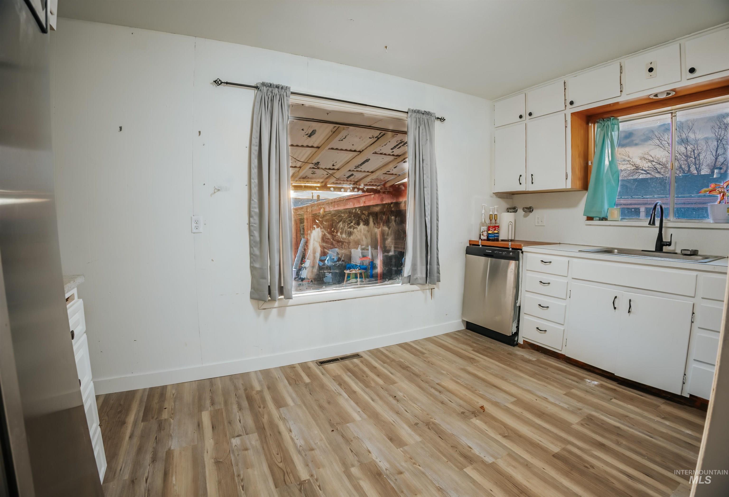Kitchen featuring white cabinetry, light countertops, light wood-style flooring, dishwasher, and plenty of natural light