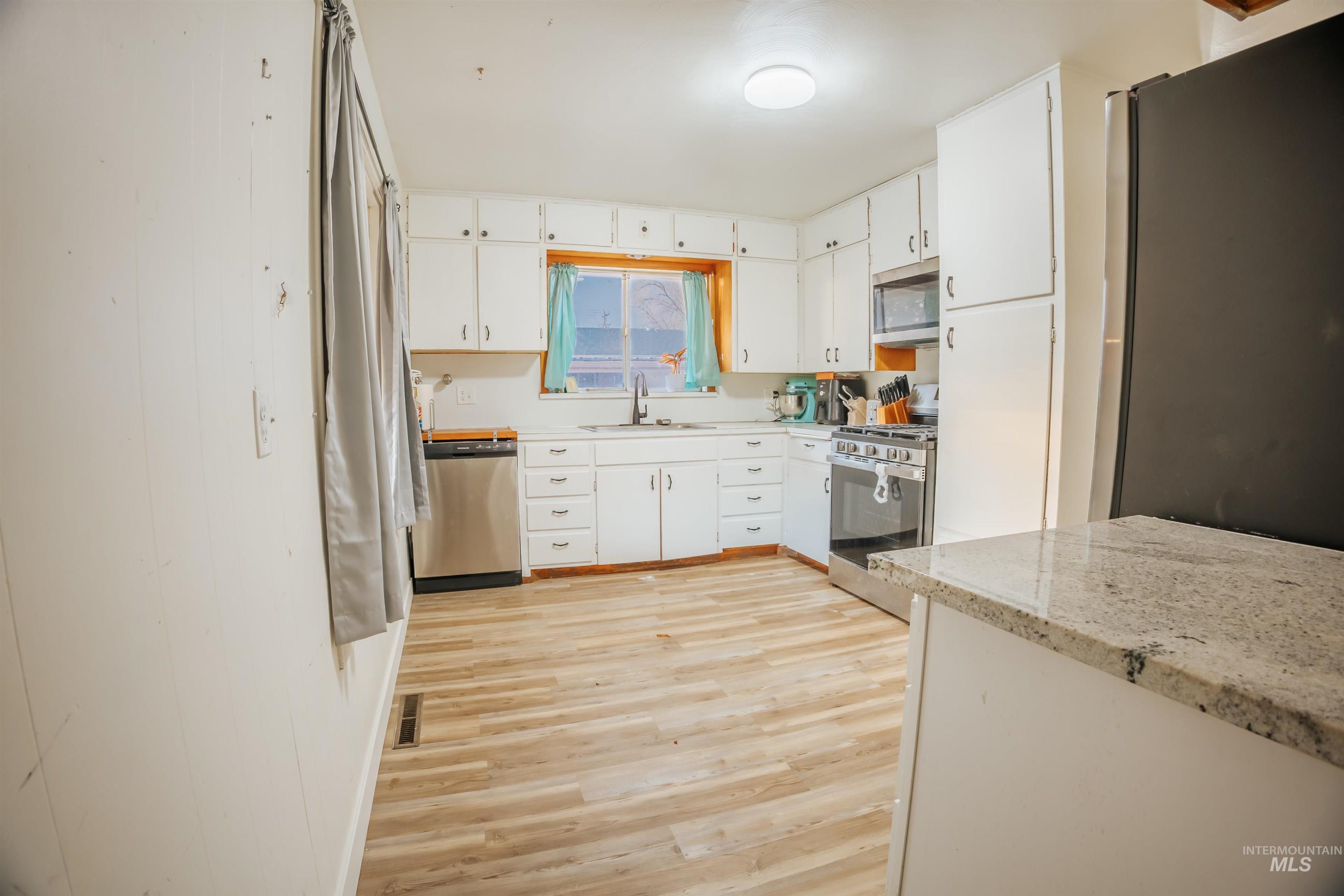 Kitchen with white cabinets, appliances with stainless steel finishes, and light wood-style floors