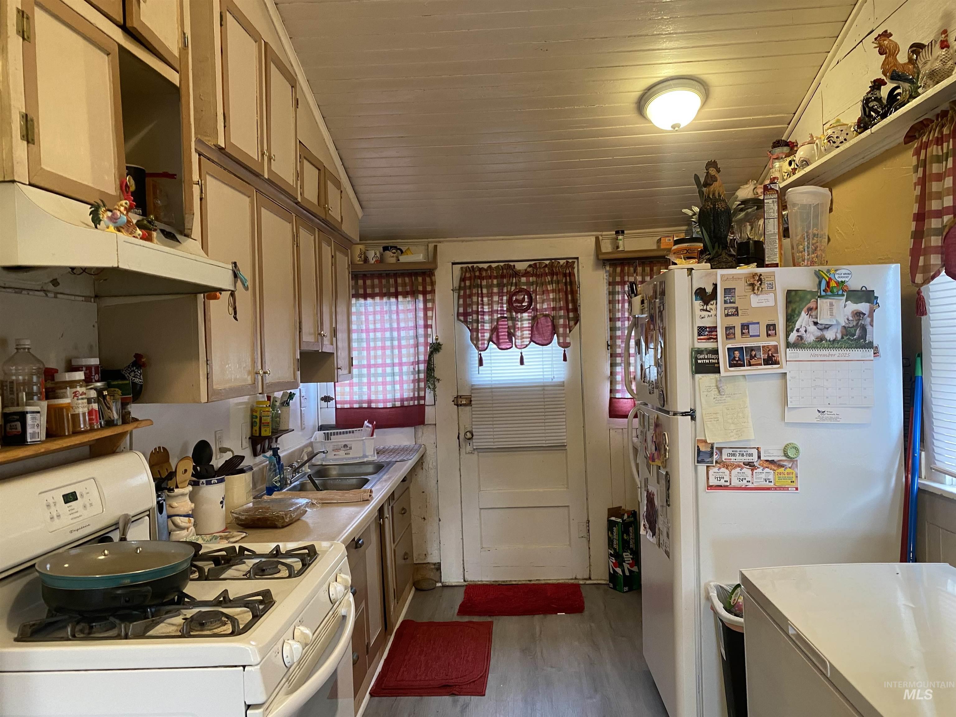 Kitchen with white appliances, light countertops, light wood finished floors, under cabinet range hood, and vaulted ceiling