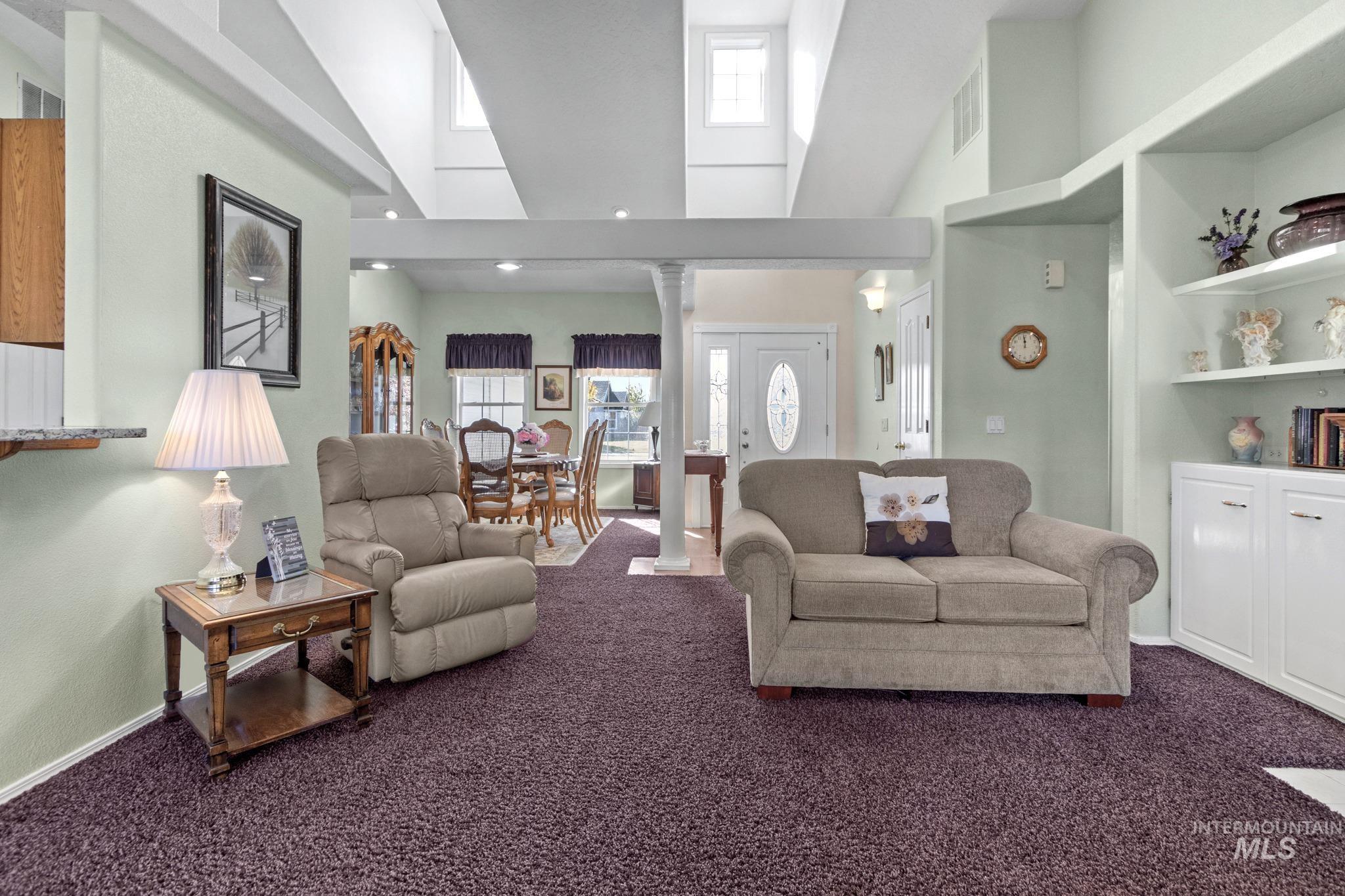 Living room featuring dark colored carpet, ornate columns, and a towering ceiling