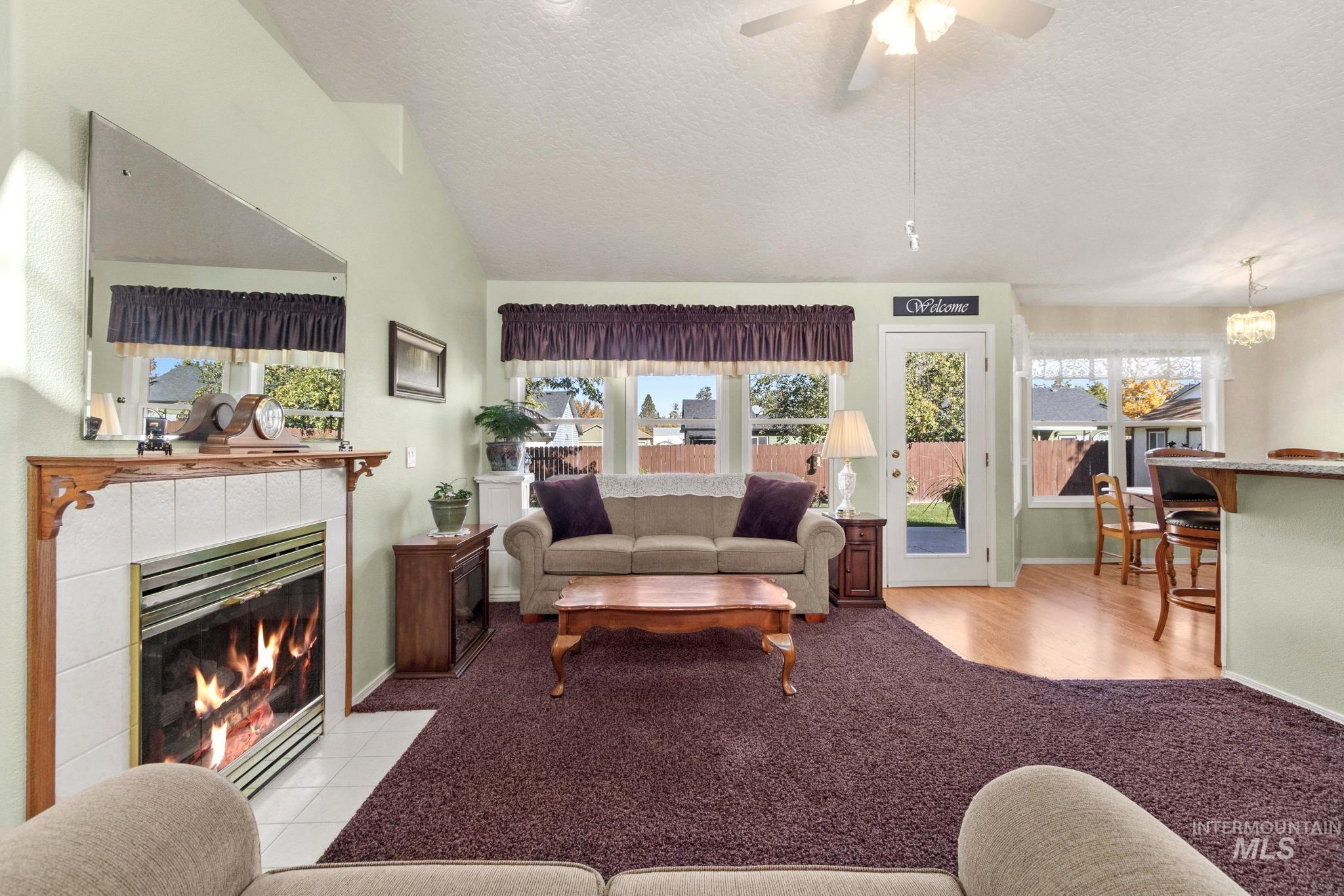 Living area with a textured ceiling, a tile fireplace, a ceiling fan, vaulted ceiling, and light carpet