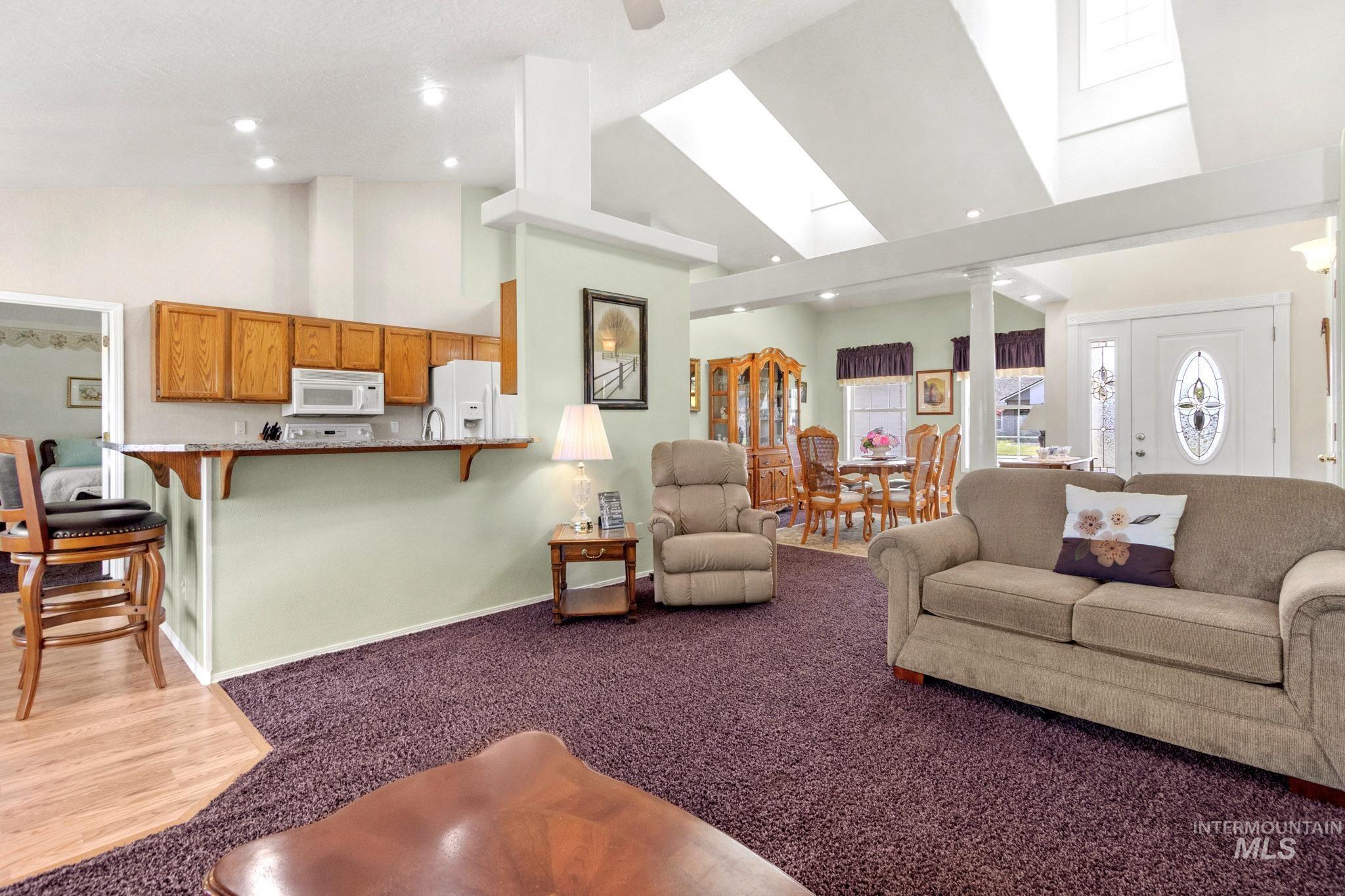 Carpeted living area with high vaulted ceiling, a skylight, and recessed lighting