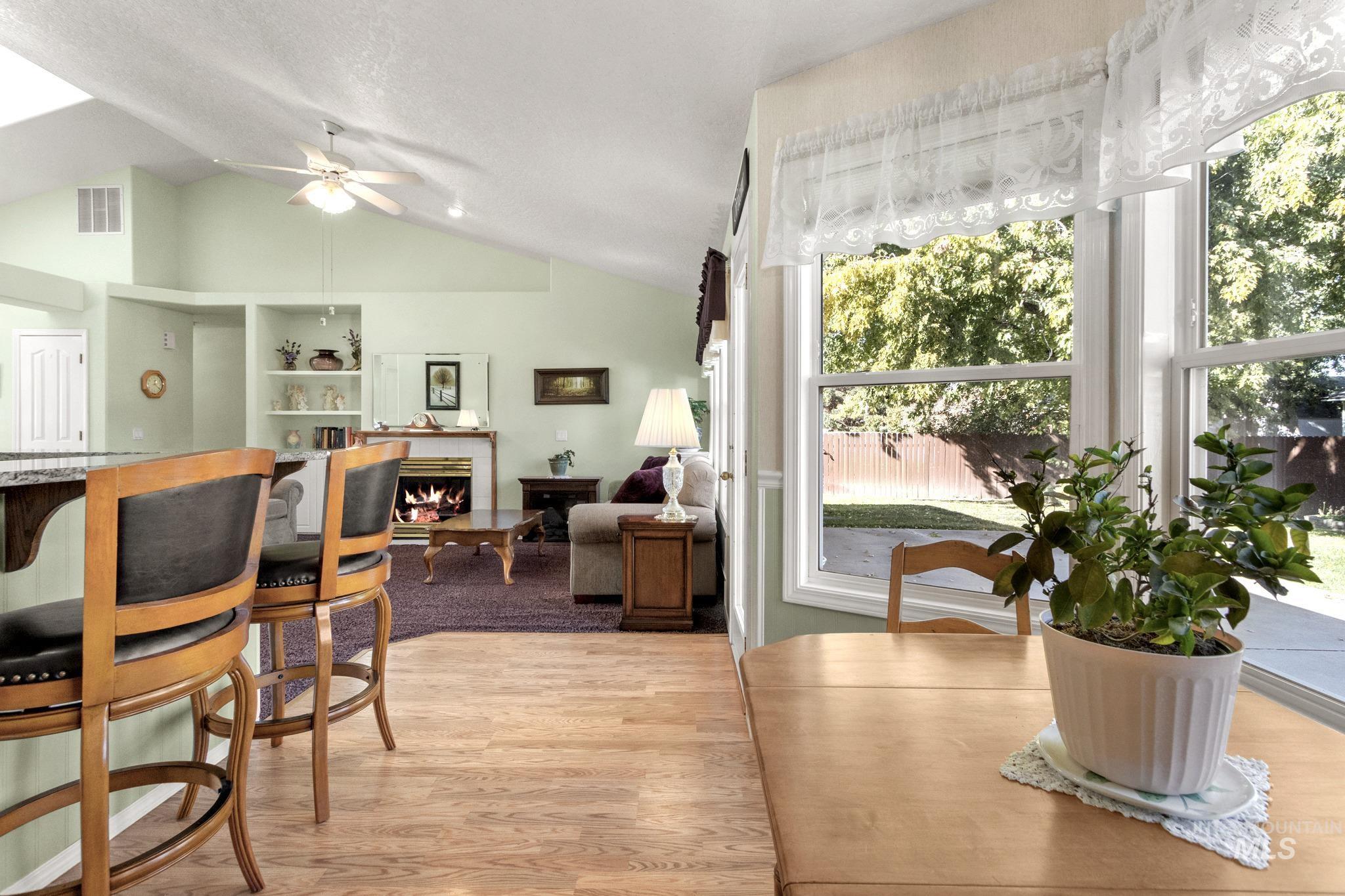 Dining area featuring a warm lit fireplace, light wood-style flooring, lofted ceiling, and ceiling fan