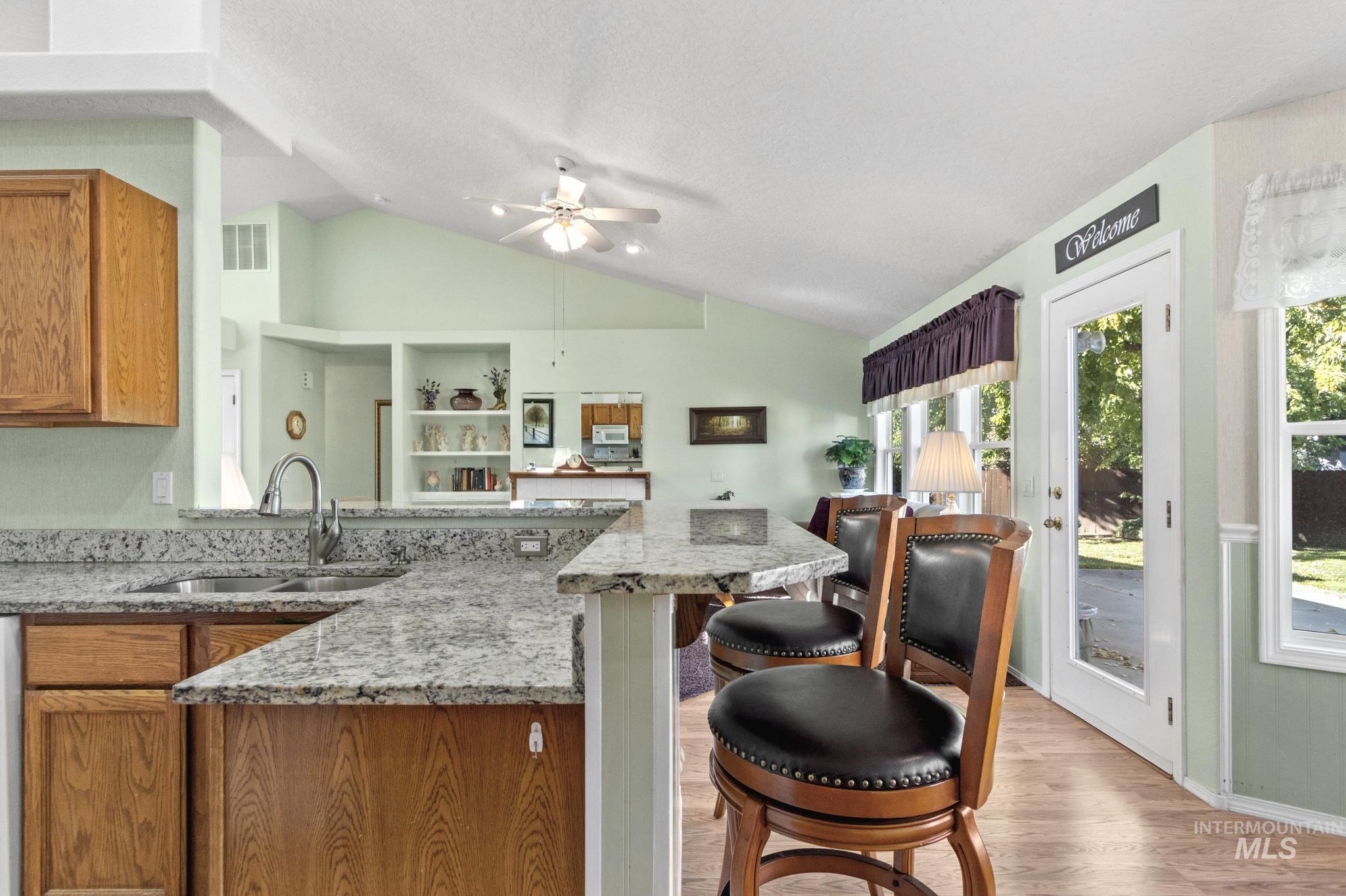 Kitchen with light stone countertops, brown cabinets, a kitchen bar, a peninsula, and vaulted ceiling
