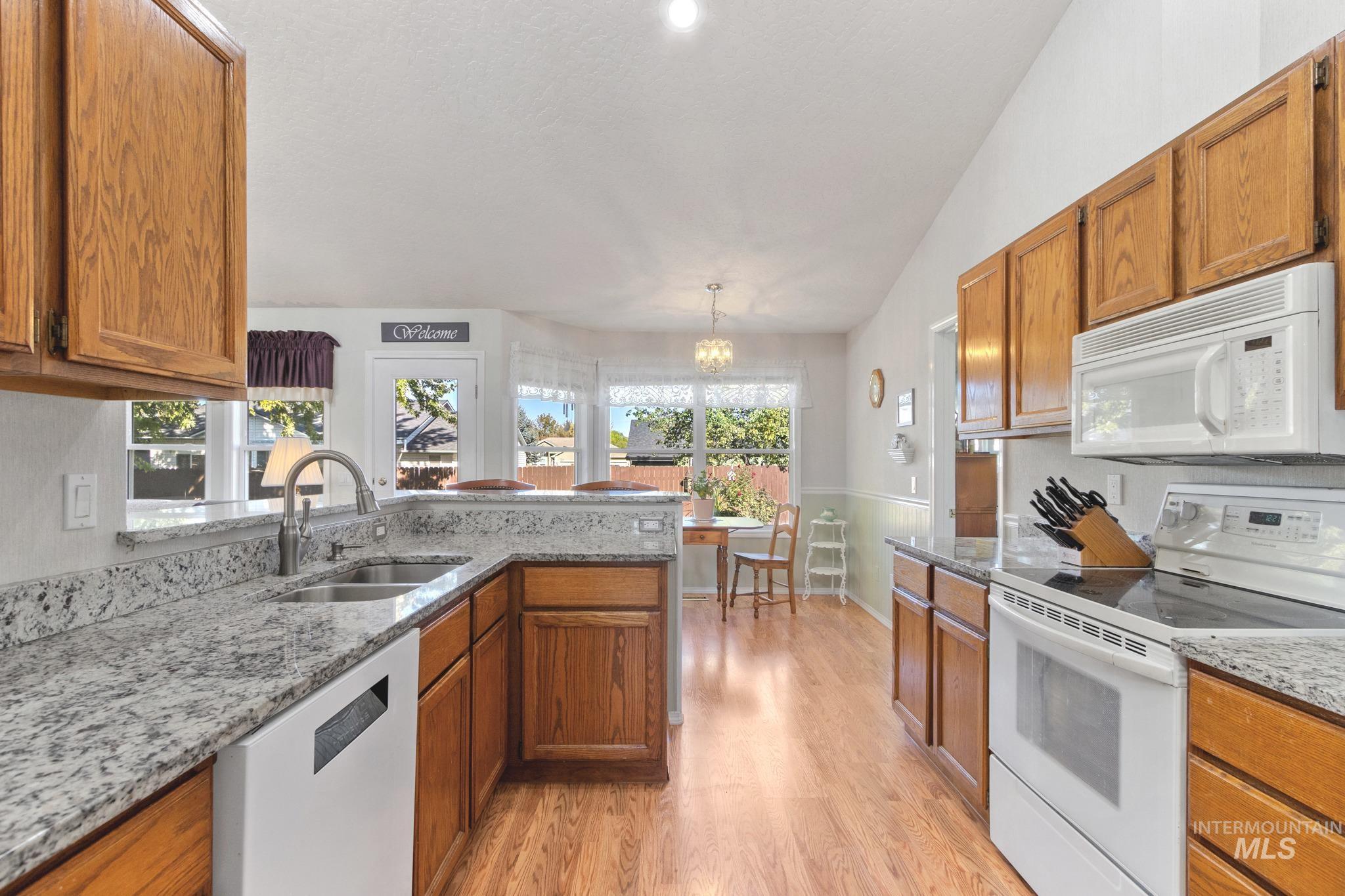 Kitchen featuring white appliances, brown cabinets, light stone countertops, a chandelier, and vaulted ceiling