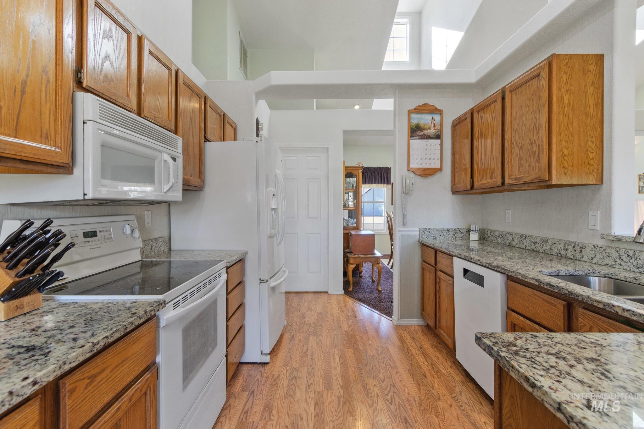 Kitchen with white appliances, brown cabinetry, light stone counters, and light wood-style flooring